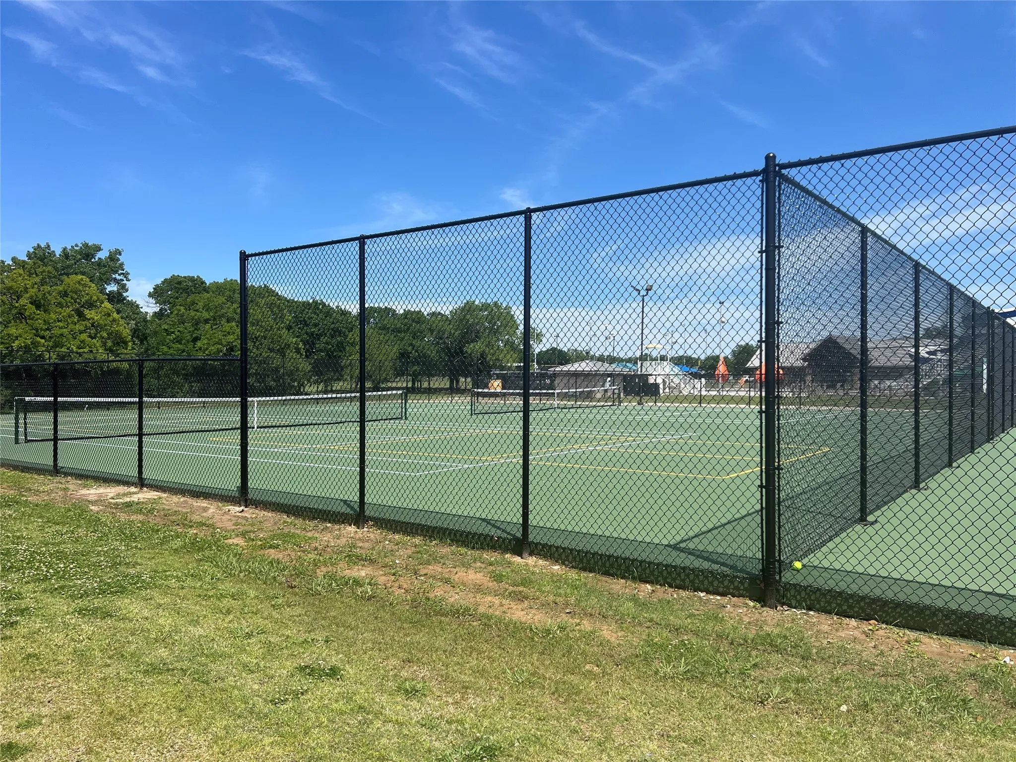 Green tennis court surrounded by black chain-link fencing