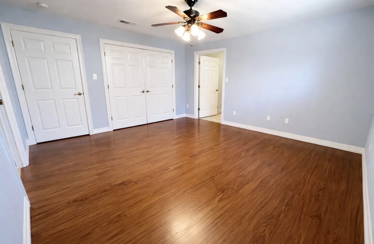 Spacious room featuring wood-finish flooring, light blue walls, and white baseboards