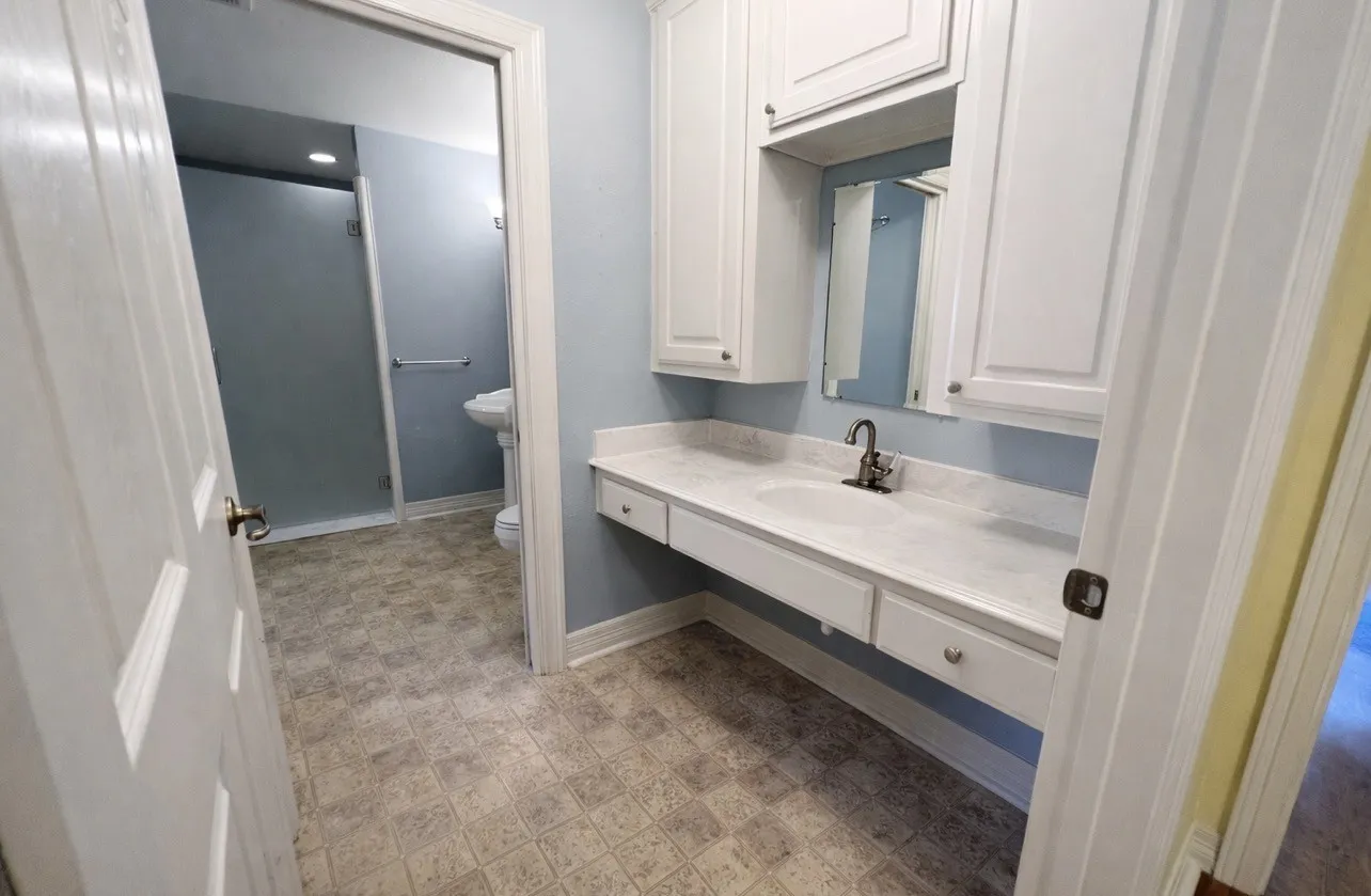 Bathroom featuring a vanity with a white countertop and integrated sink, white cabinetry with silver hardware, a mirror, and an adjacent shower enclosure with a clear glass door