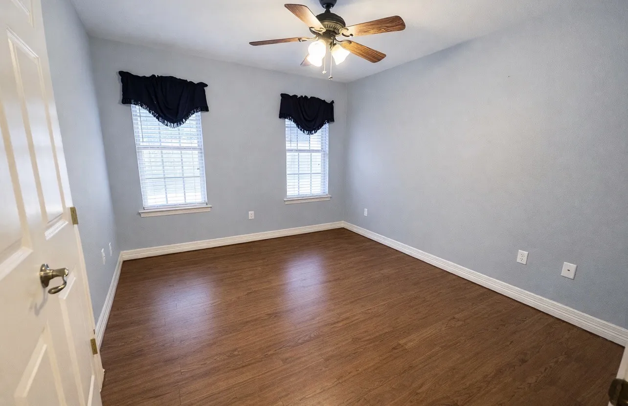 Room featuring wood-finish flooring, two windows with blinds, a ceiling fan with integrated lighting, light-toned wall finishes, and white baseboards