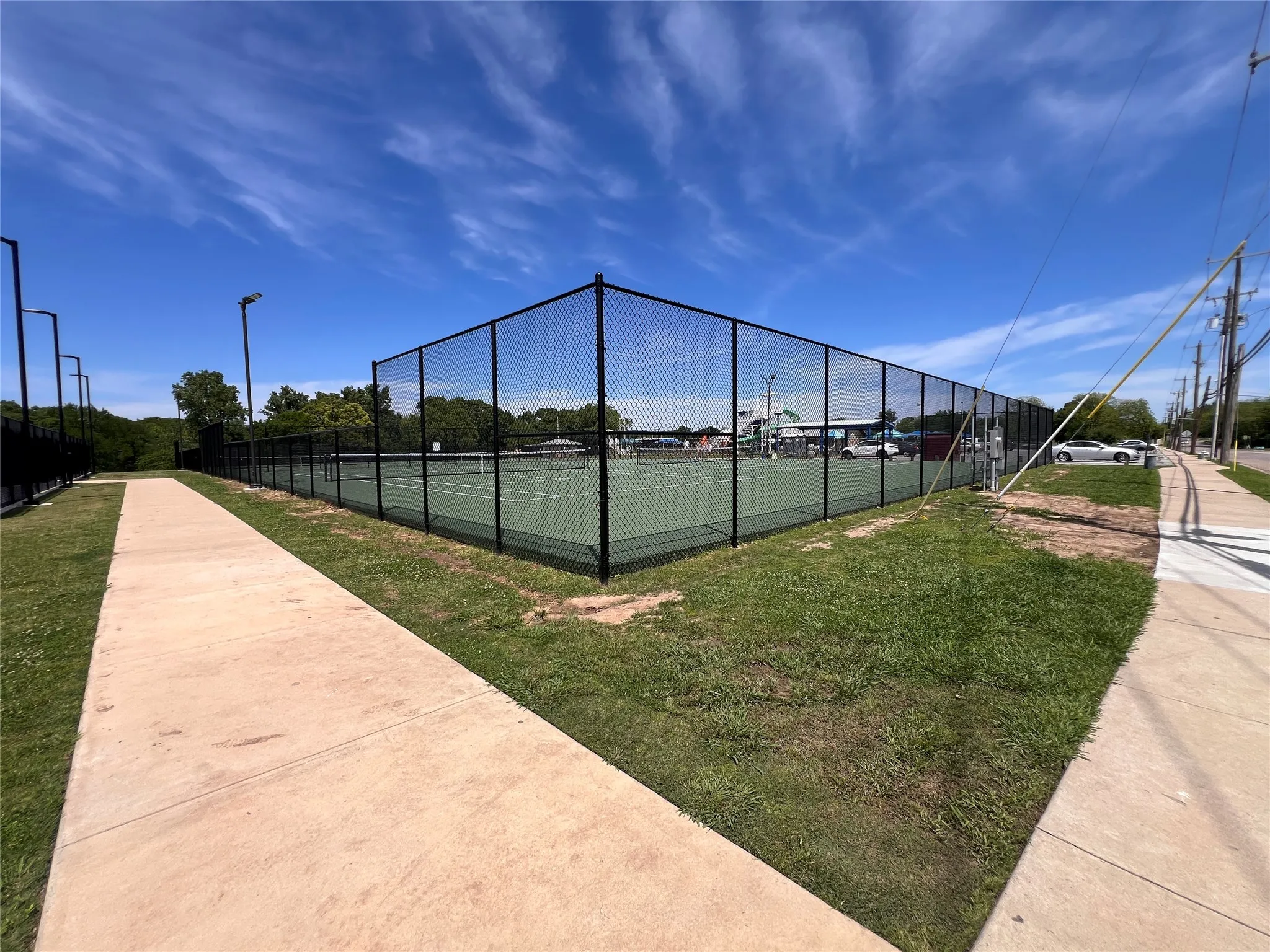 Regulation-size tennis court featuring black chain-link fencing, a hard court surface, and perimeter lighting