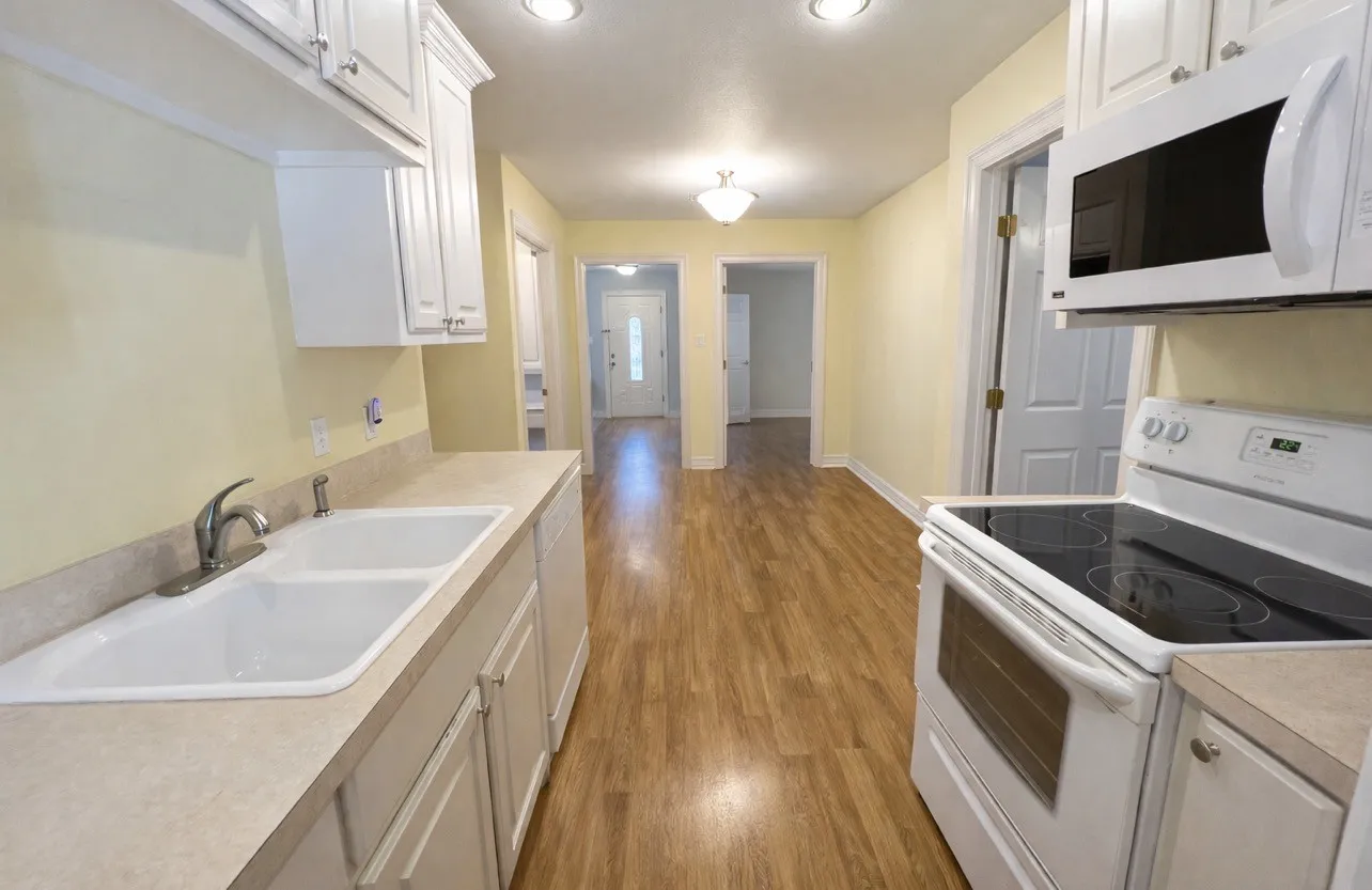 Kitchen featuring white cabinetry, a double basin sink, light-colored countertops, and wood-finish flooring