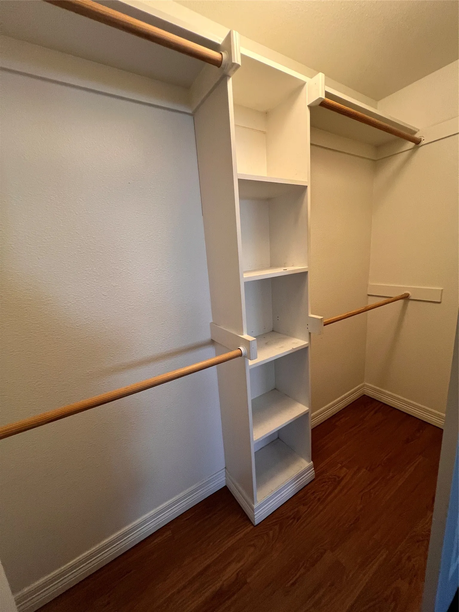 Wardrobe featuring built-in shelving, multiple hanging rods, white trim, and wood-finish flooring
