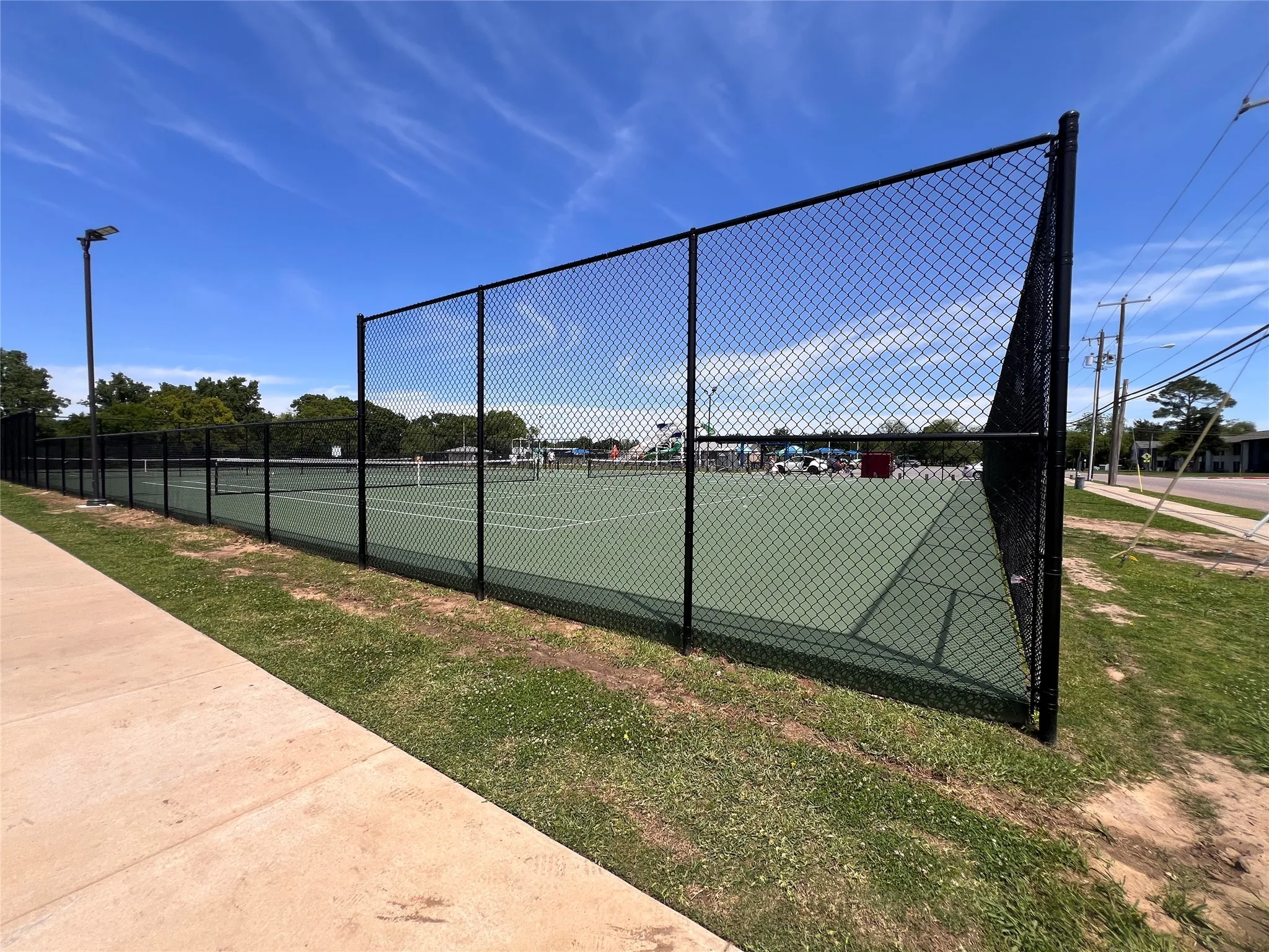 Outdoor tennis court featuring a green playing surface and perimeter fencing
