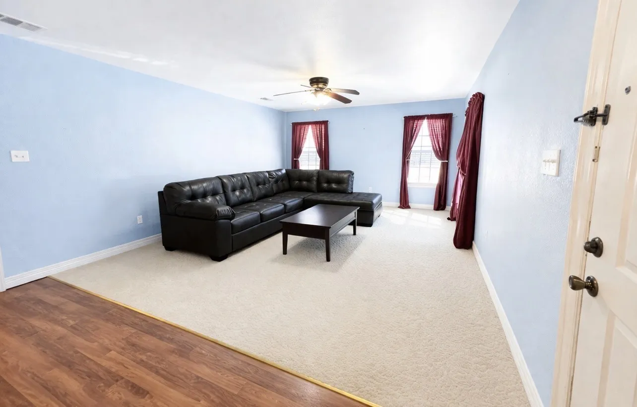 Spacious living area featuring light blue painted walls, neutral carpet flooring, and a wood-finish flooring entry