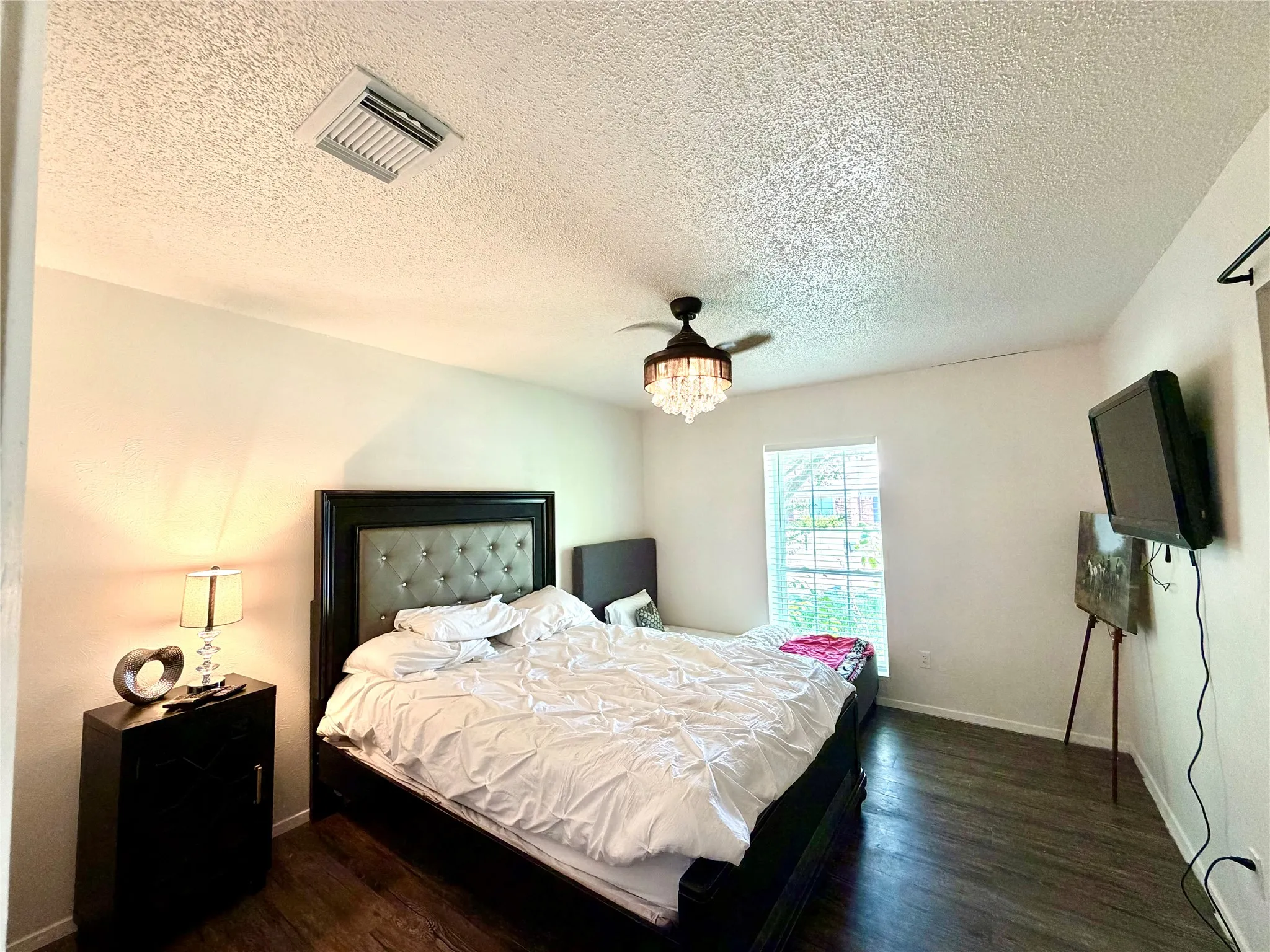 Bedroom featuring wood-finish flooring, a contemporary chandelier fan, a window with horizontal blinds, and textured ceilings