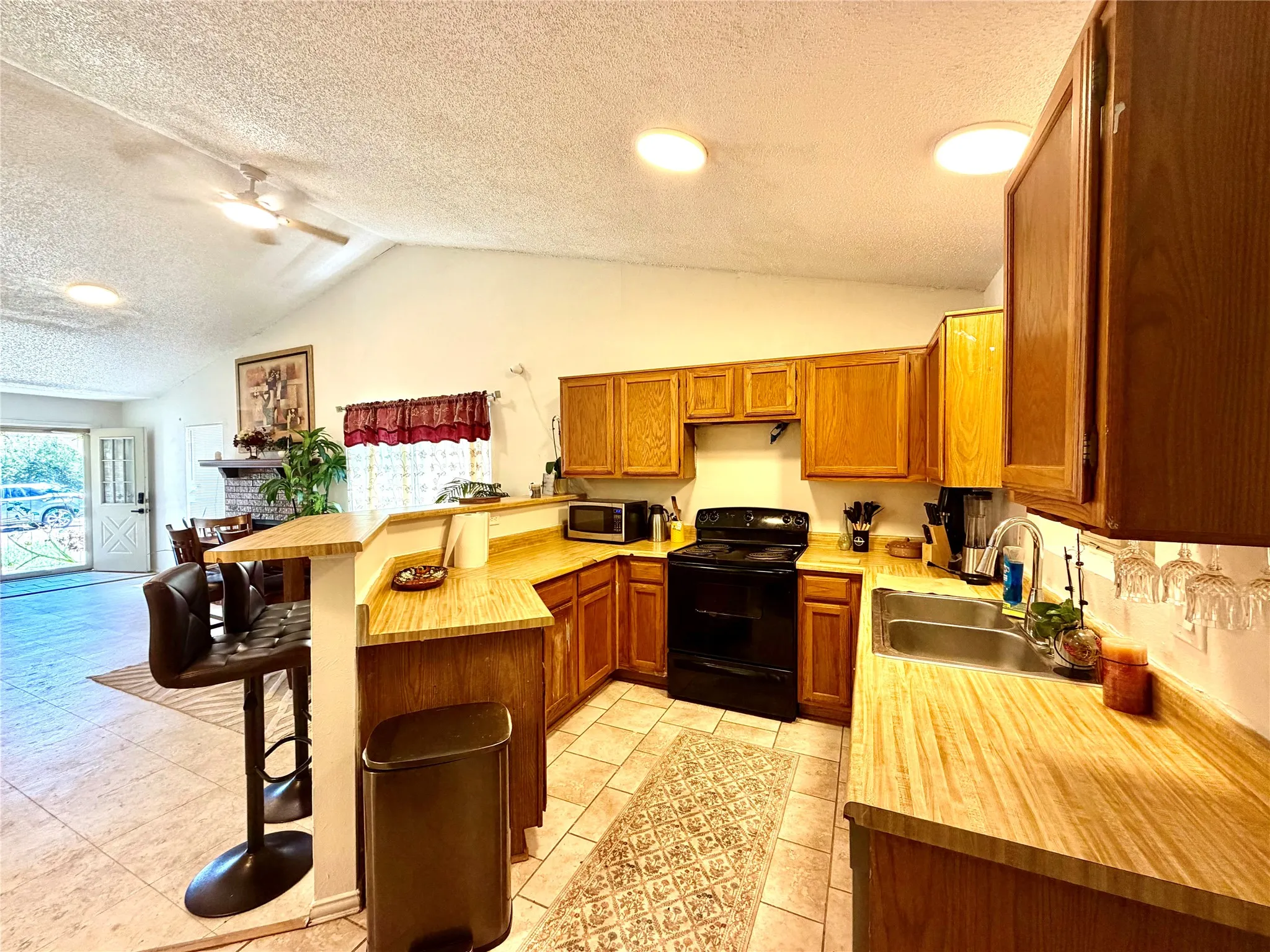 Open-concept kitchen featuring wood-finish cabinetry, light wood-finish countertops, and a black appliance suite
