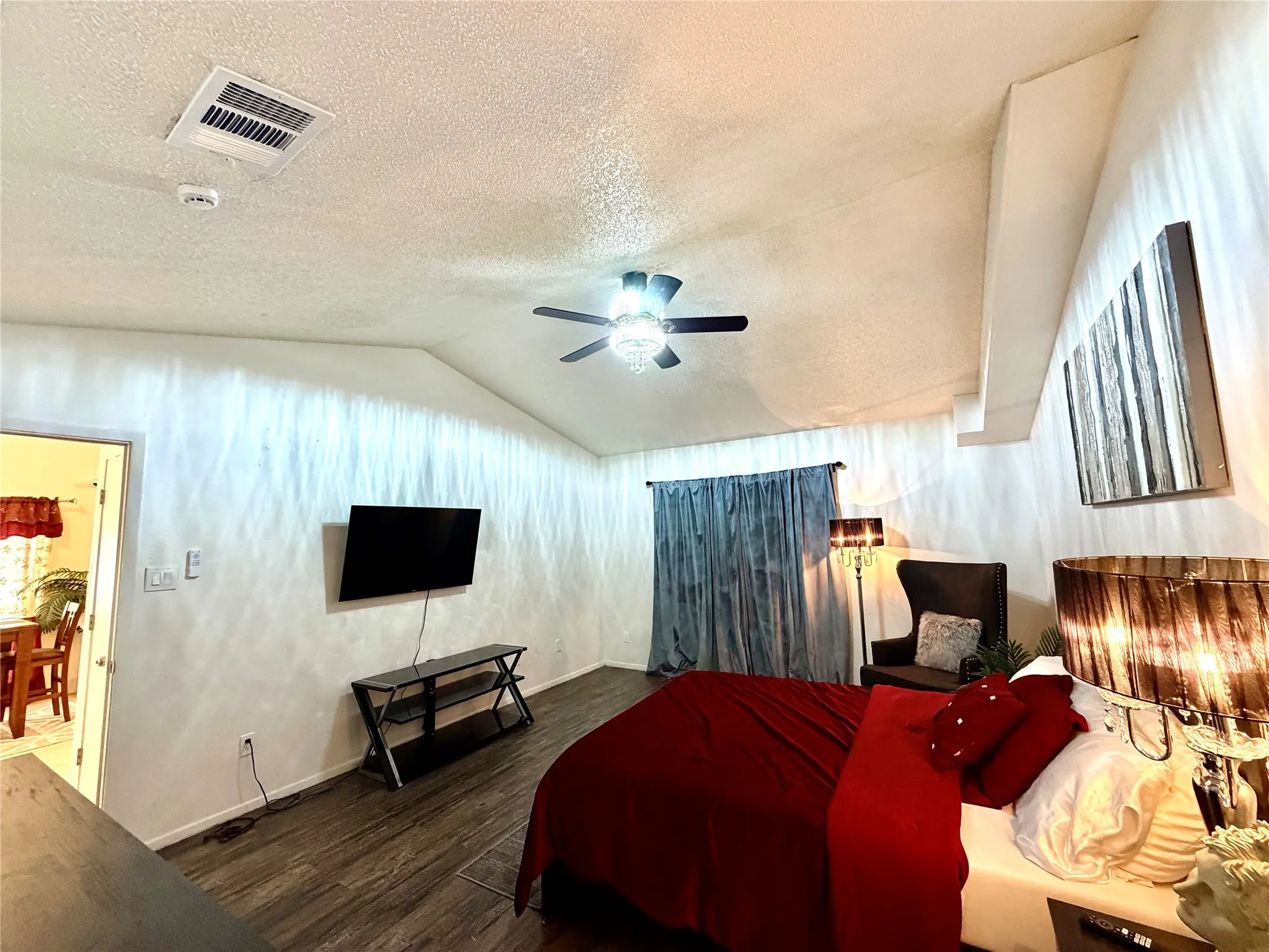 Vaulted ceiling bedroom featuring wood-finish flooring, a ceiling fan with integrated lighting, and a wall-mounted television