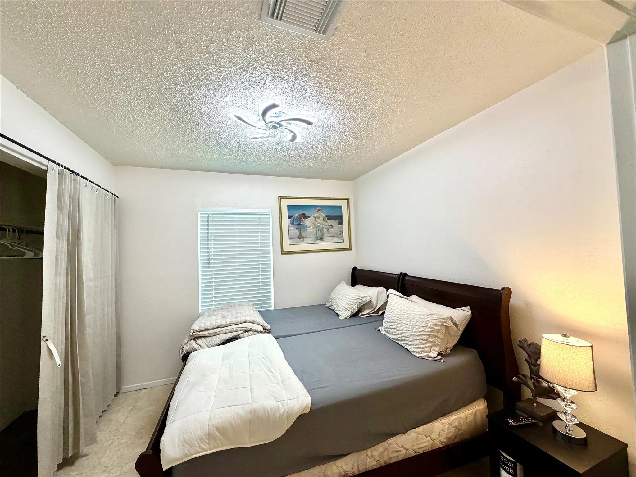 Bedroom featuring a window with horizontal blinds, overhead flush-mount lighting, and a closet with a curtain closure