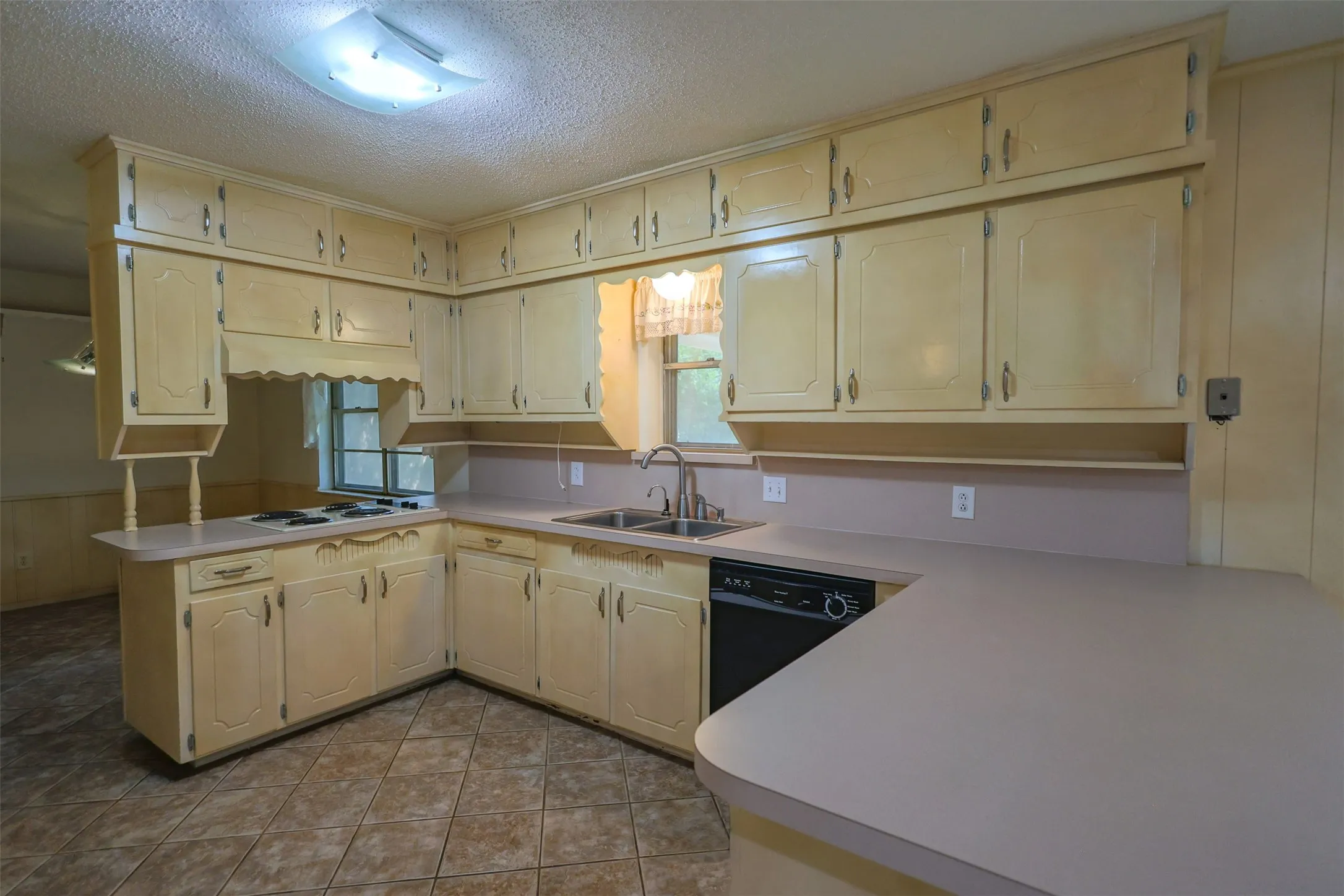 Kitchen featuring extensive upper and lower cabinetry, a built-in cooktop, a double basin sink with a chrome faucet, a black dishwasher, and a breakfast bar