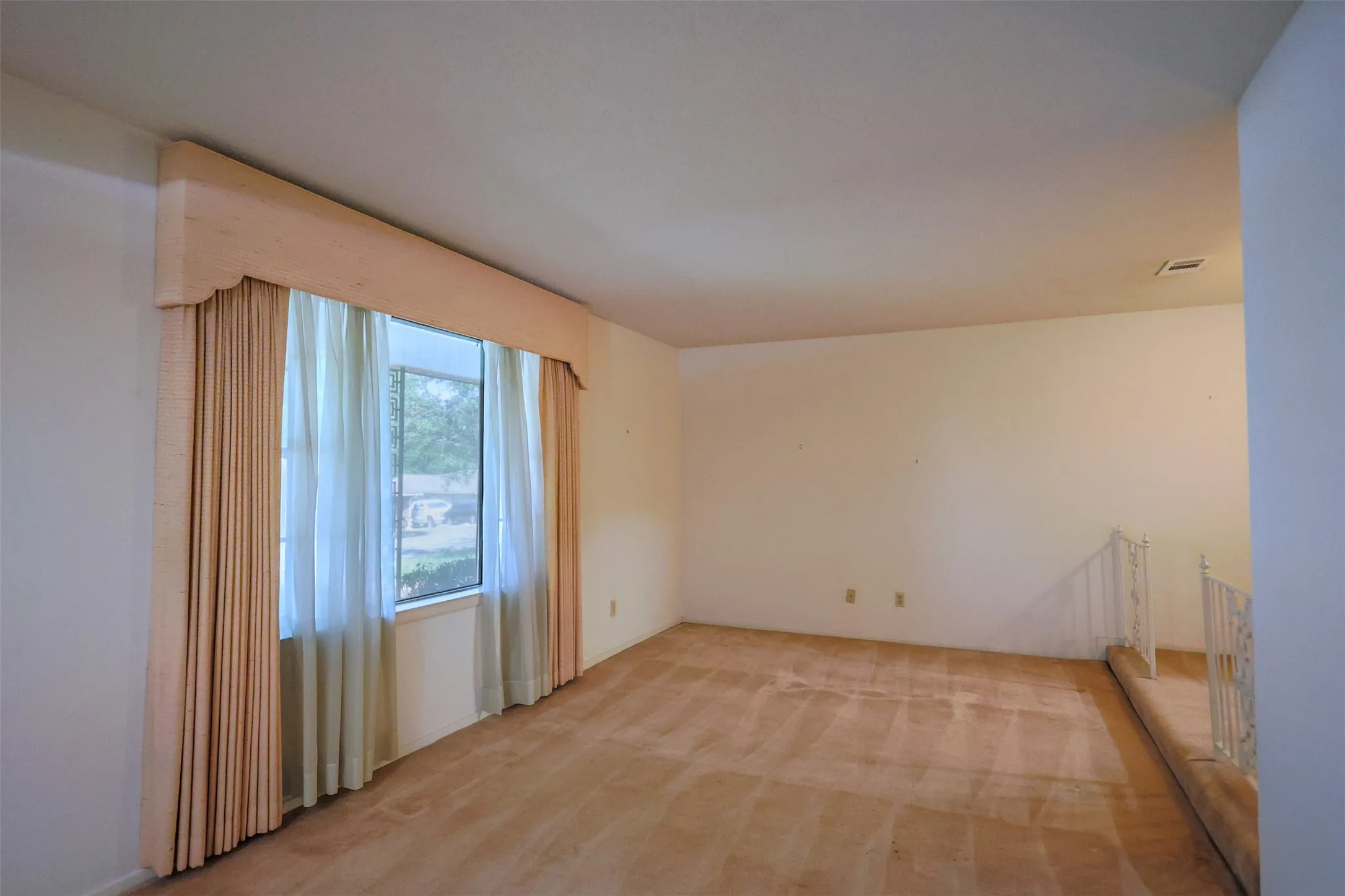 Spacious room with a large window and neutral-toned carpeting