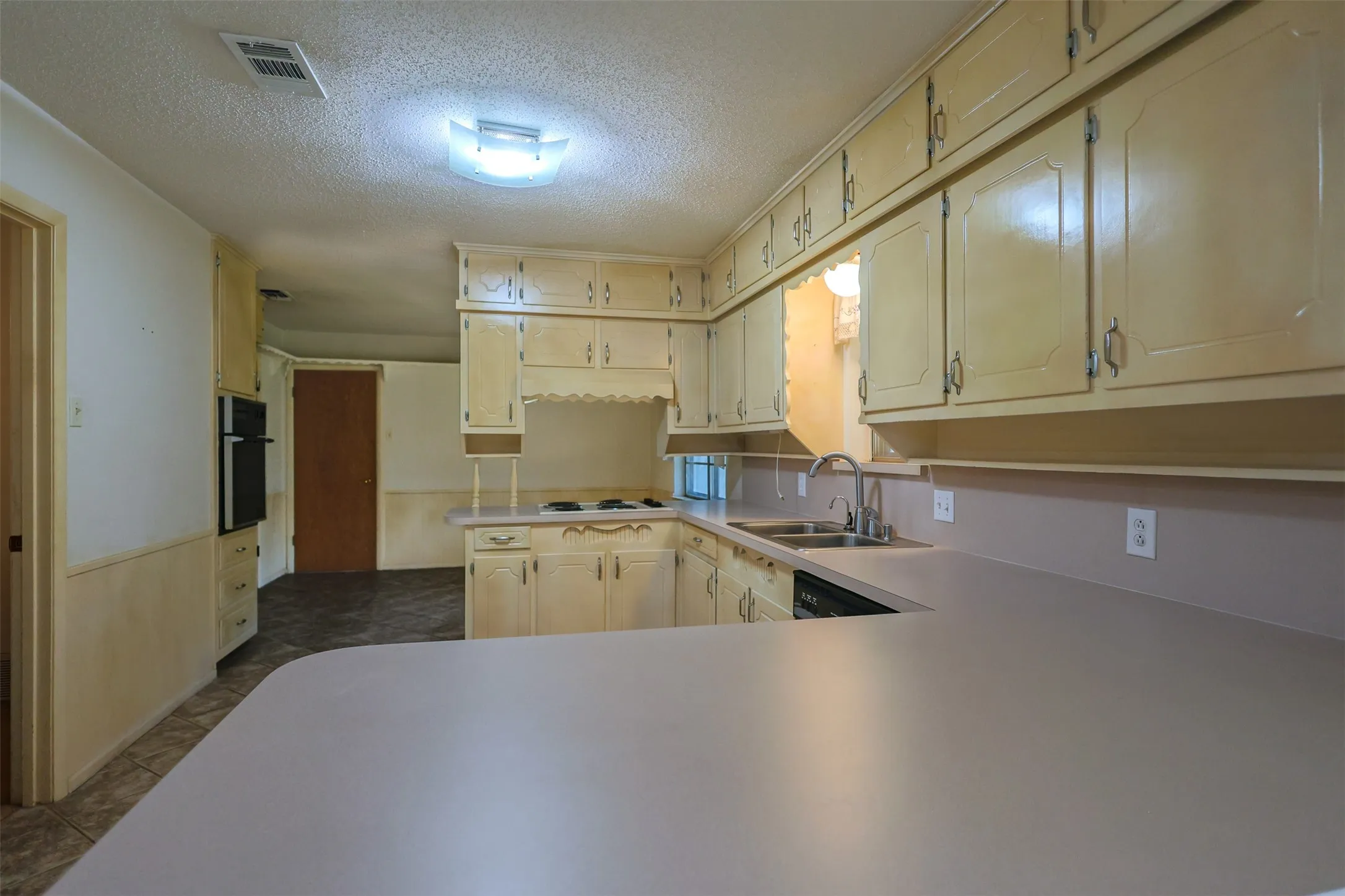 U-shaped kitchen featuring extensive cabinetry, a built-in oven, and a double basin sink with a single-handle faucet