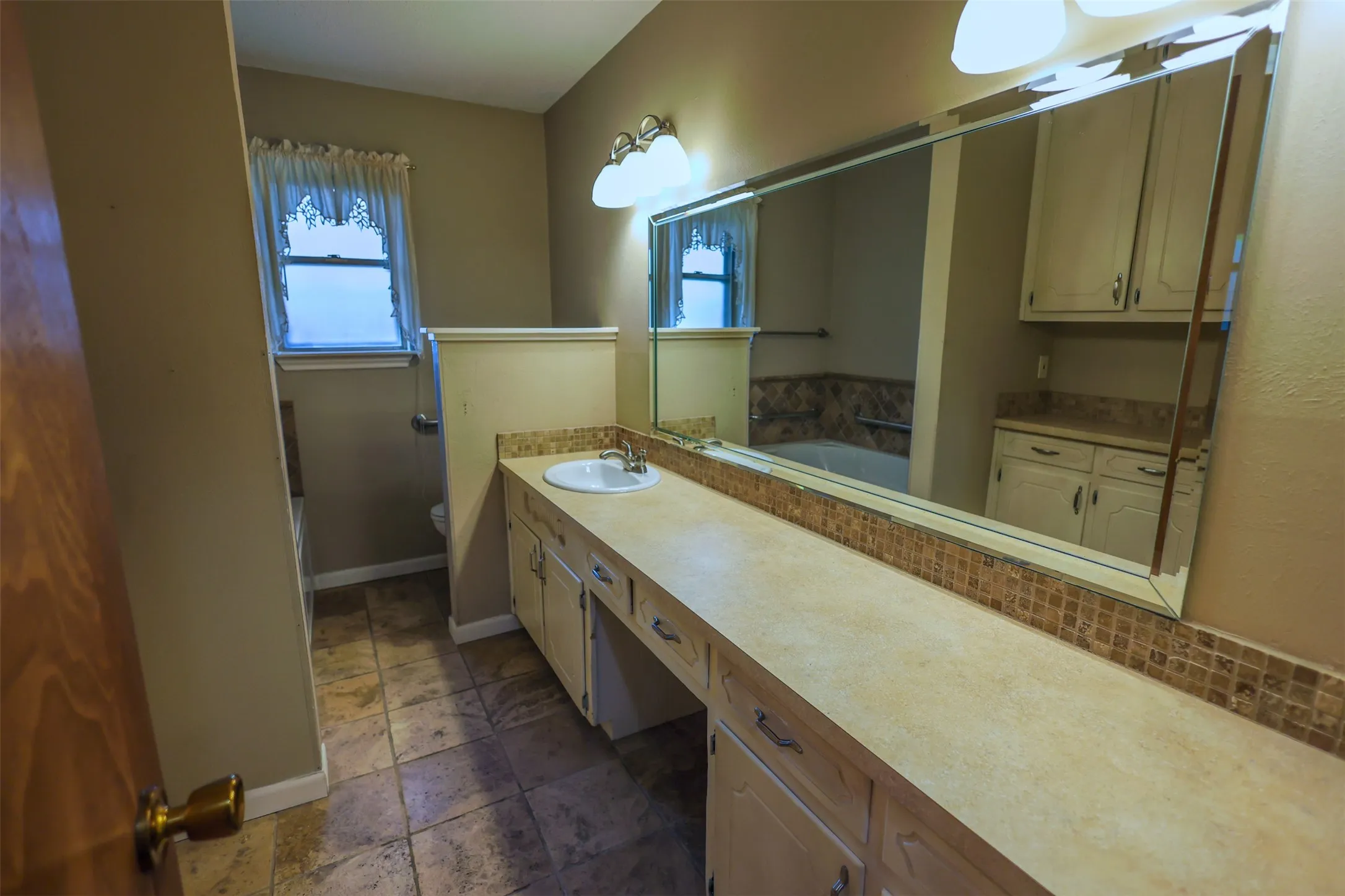 Bathroom featuring an extended vanity with an integrated sink, ample storage cabinetry, and a full-width mirror