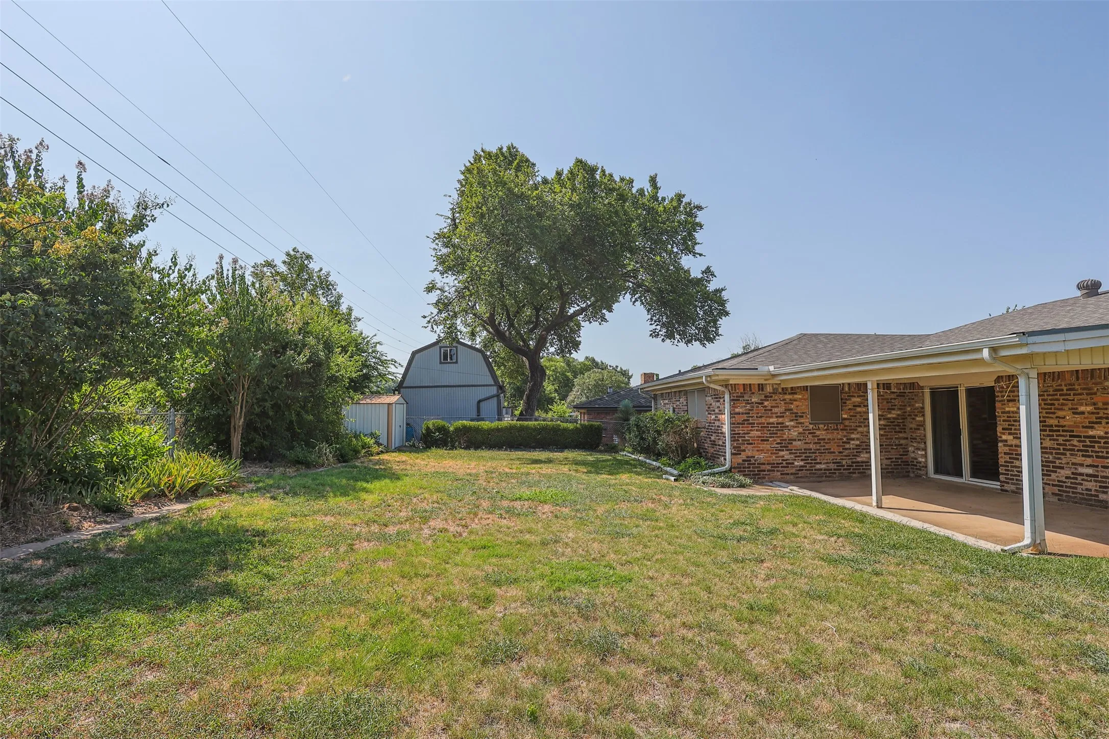Expansive backyard featuring a covered patio, brick exterior, mature trees, and a detached barn-style shed