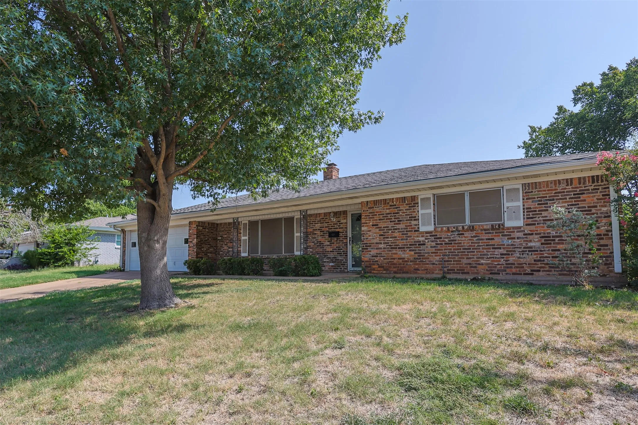 Brick facade with white shutters, a covered entry, and an attached garage
