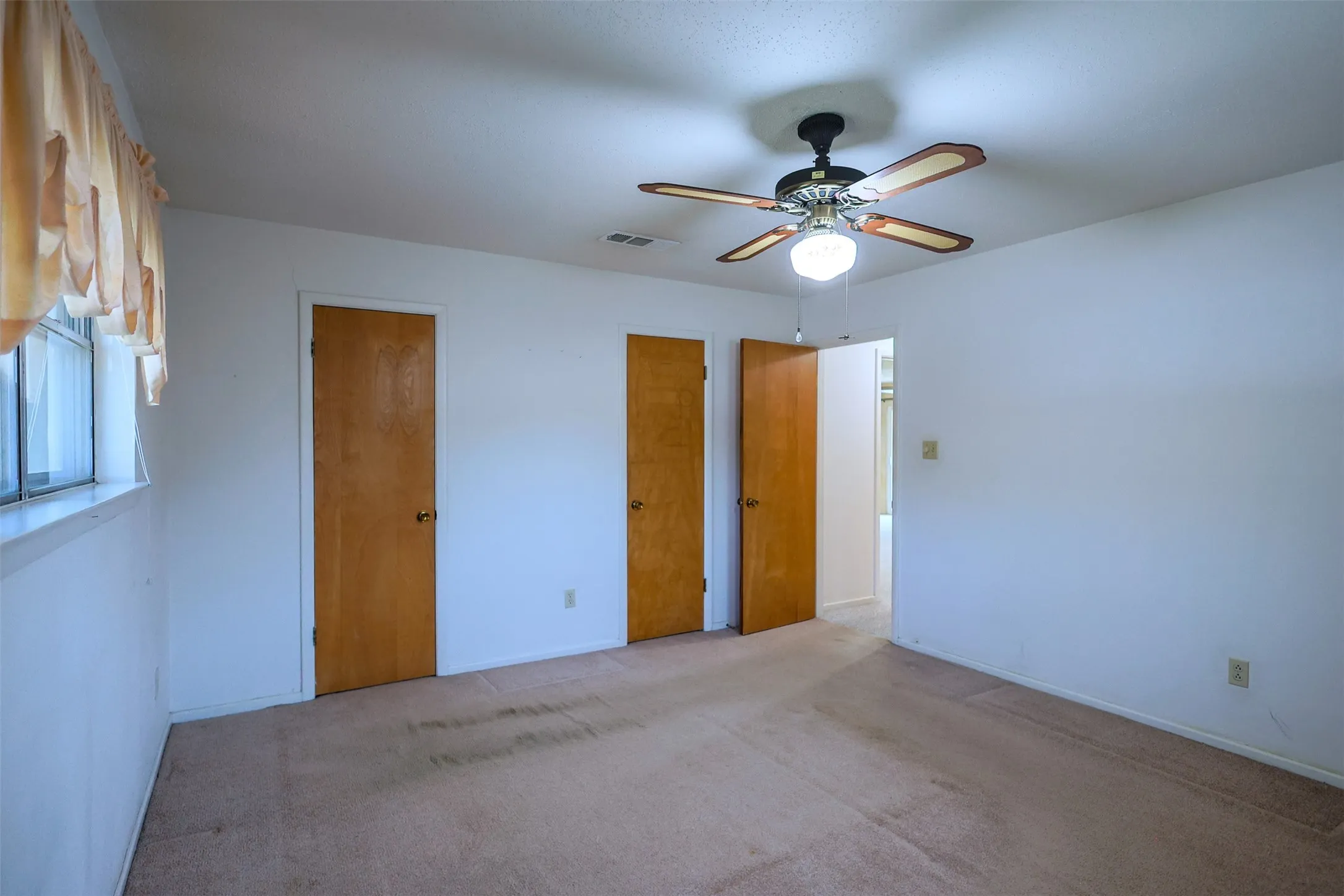 Carpeted room with a ceiling fan light fixture, white painted walls, and wood-paneled doors