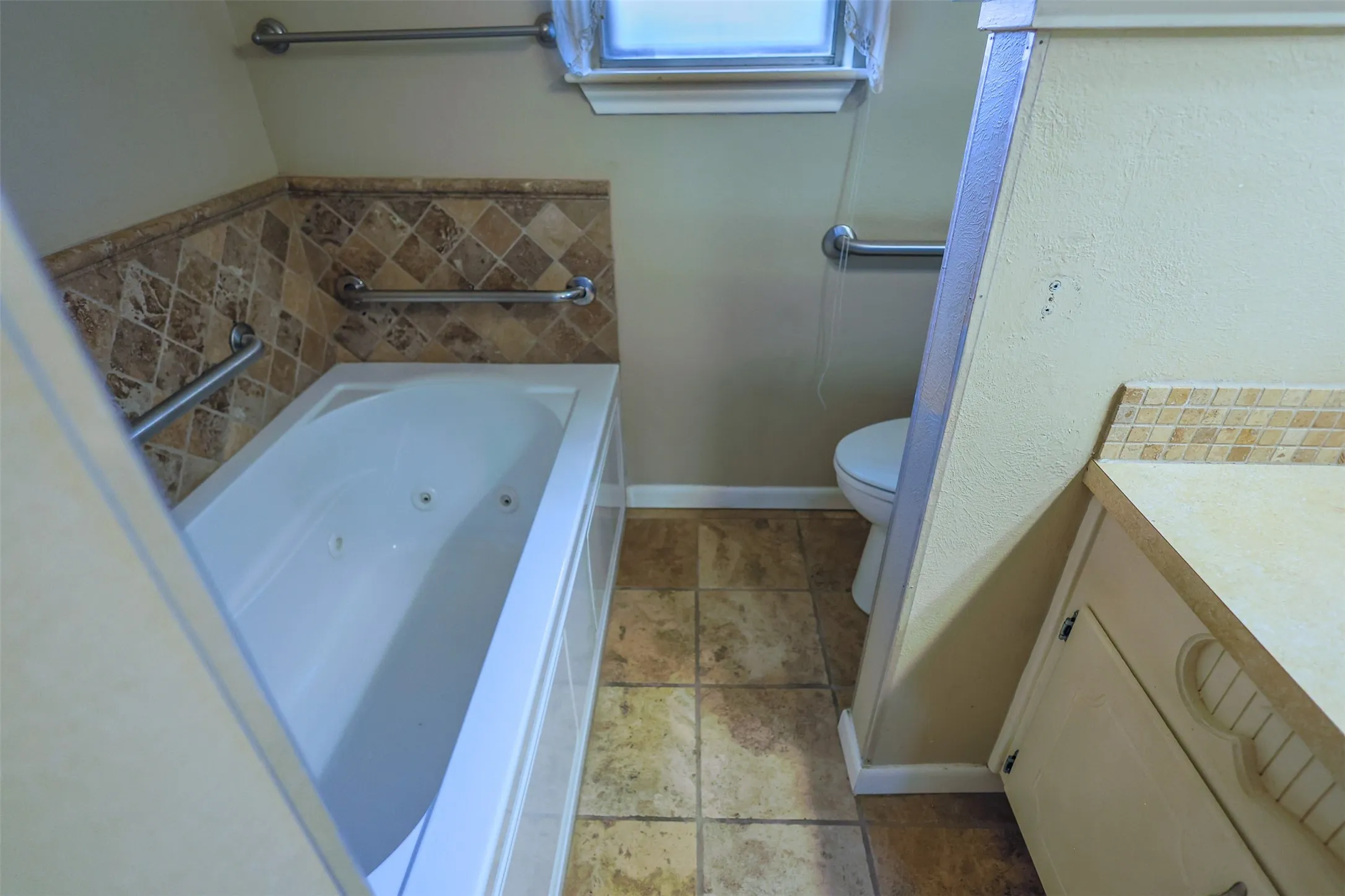 Bathroom featuring a jetted tub with grab bars, decorative tile surround, and tile flooring