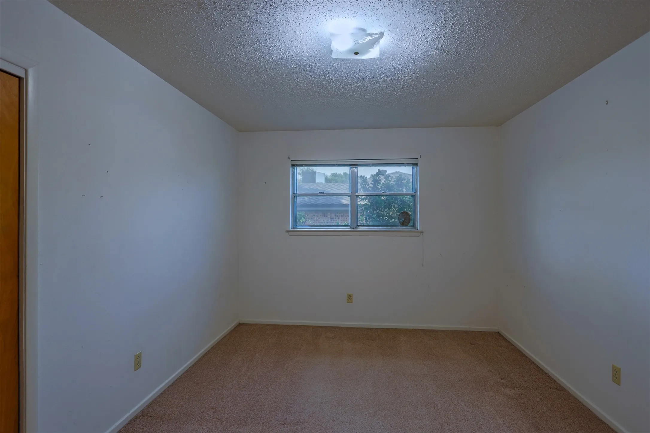 Carpeted interior room featuring a window, overhead flush mount lighting, and a wood-finish door frame
