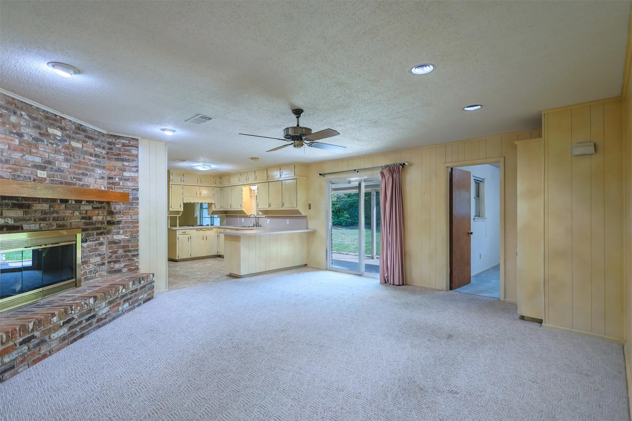 Spacious living area featuring a brick fireplace with a wood mantle, carpeted flooring, and recessed lighting