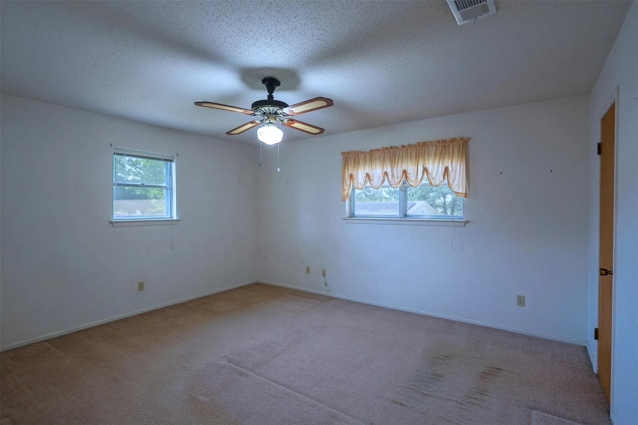 Carpeted room featuring a ceiling fan with light fixture, two windows, and white walls