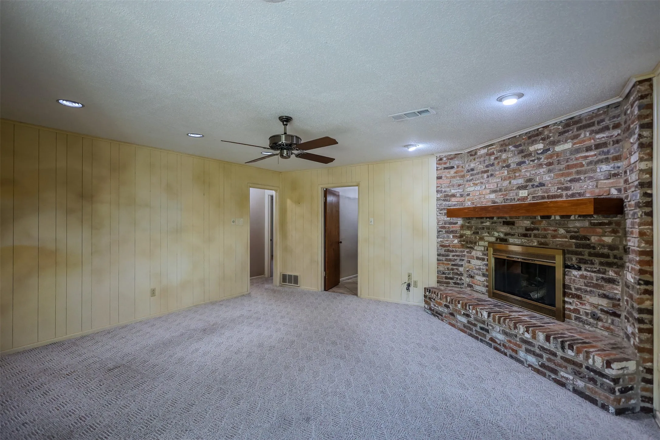 Room featuring a brick fireplace with a wood mantle, paneled walls, recessed lighting, a ceiling fan, and patterned carpet flooring
