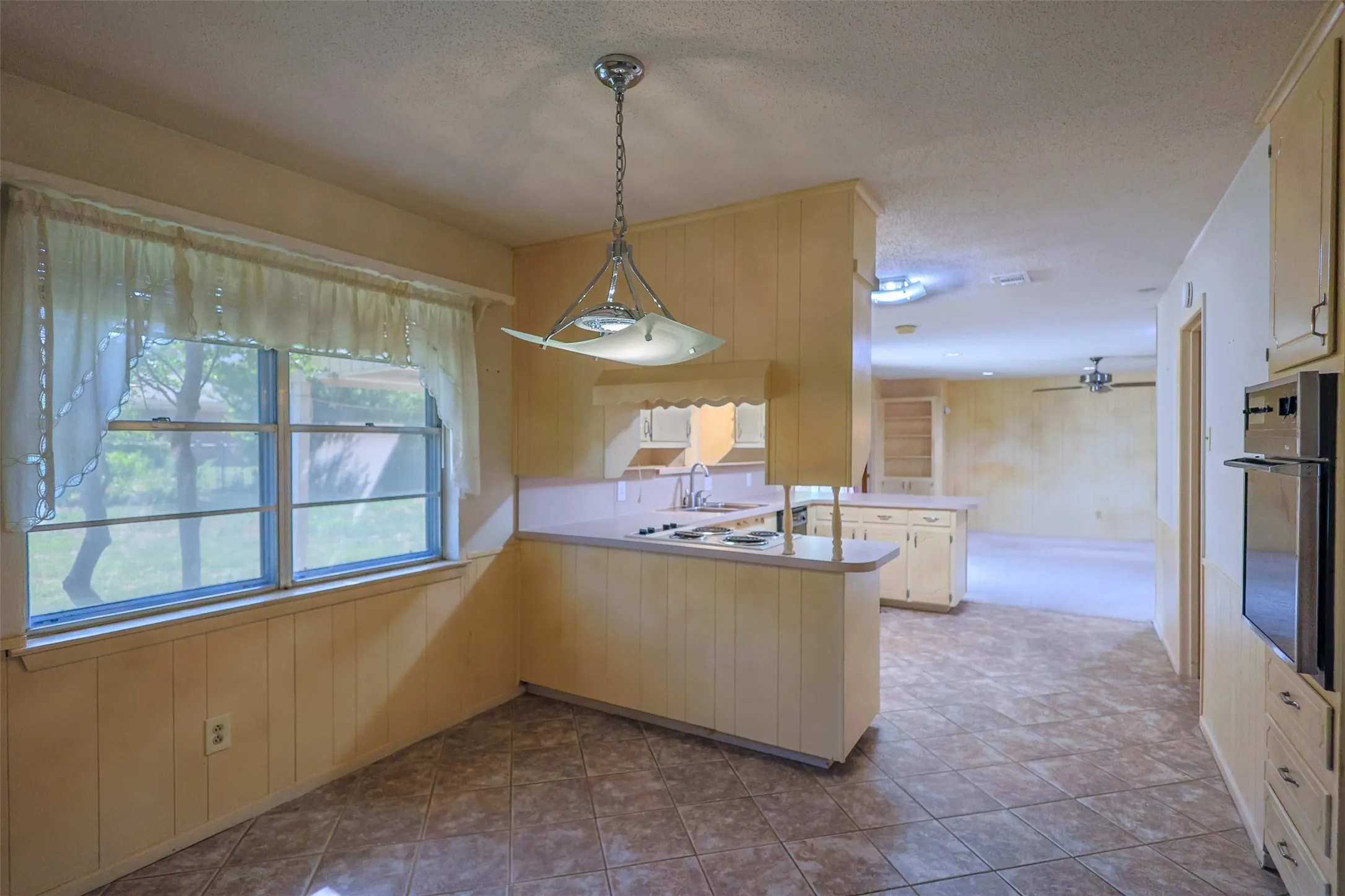 Kitchen area featuring ceramic tile flooring, a built-in electric cooktop, a wall oven, cream cabinetry, and a double window