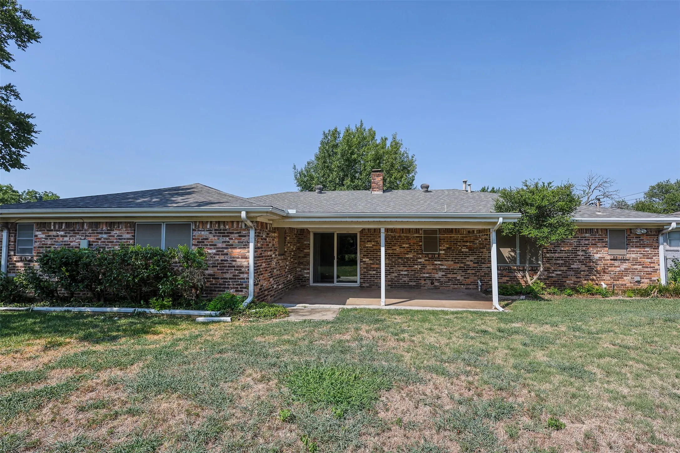 Brick exterior featuring a covered patio, sliding glass door, and a shingle roof