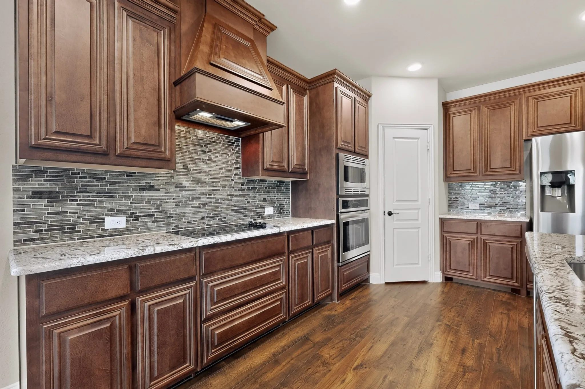 Kitchen featuring rich wood cabinetry, stone countertops, a mosaic tile backsplash, stainless steel appliances, and wood-finish flooring