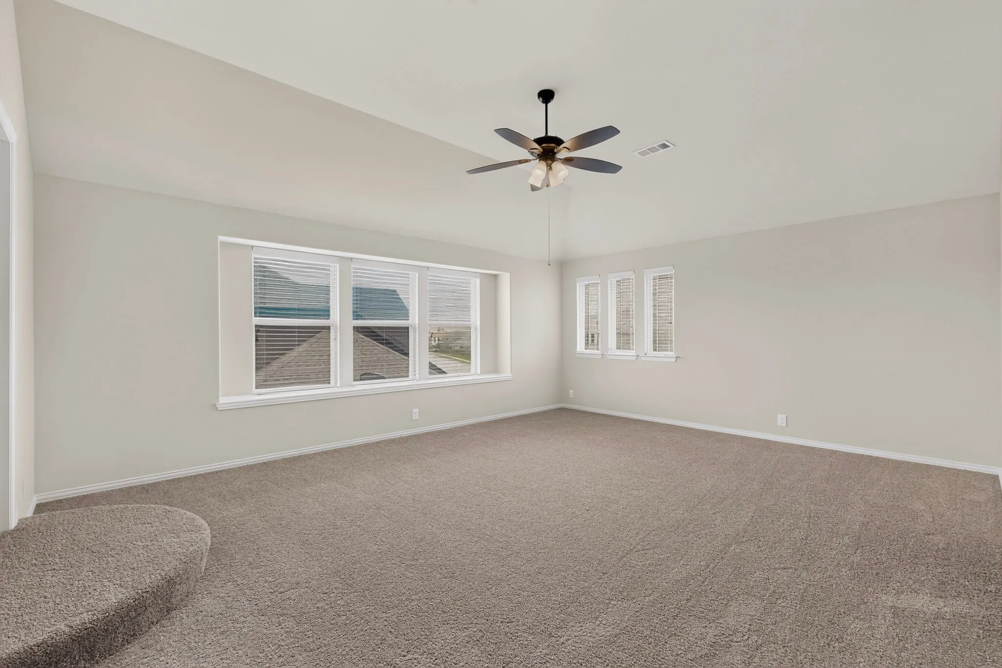 Spacious carpeted room featuring a vaulted ceiling and a ceiling fan