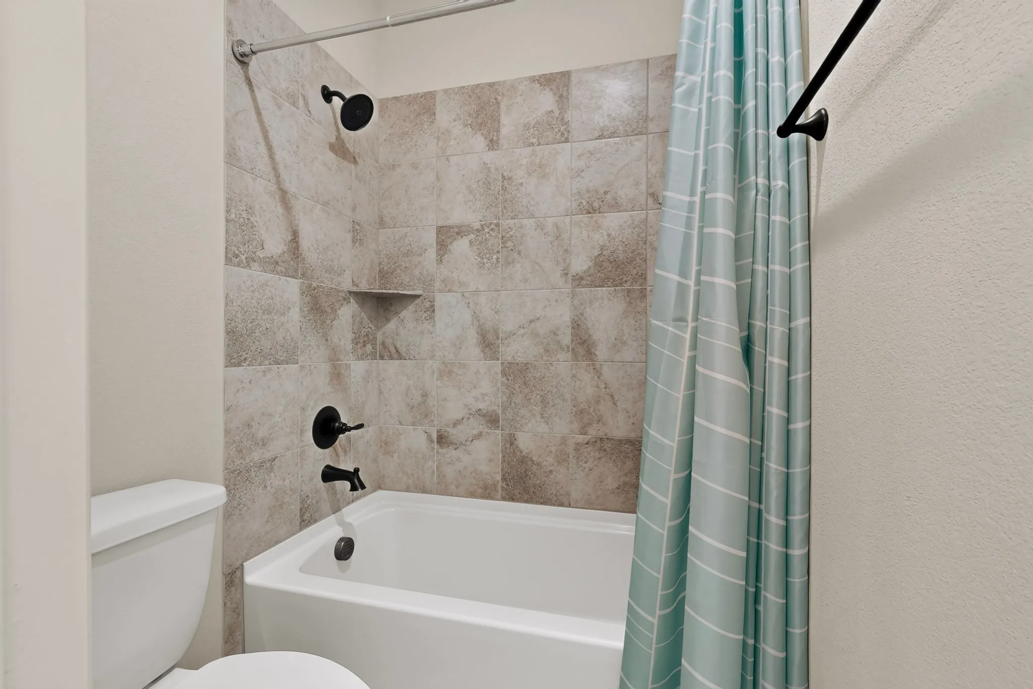 Bathtub with tile surround featuring a built-in shower niche and matte black fixtures