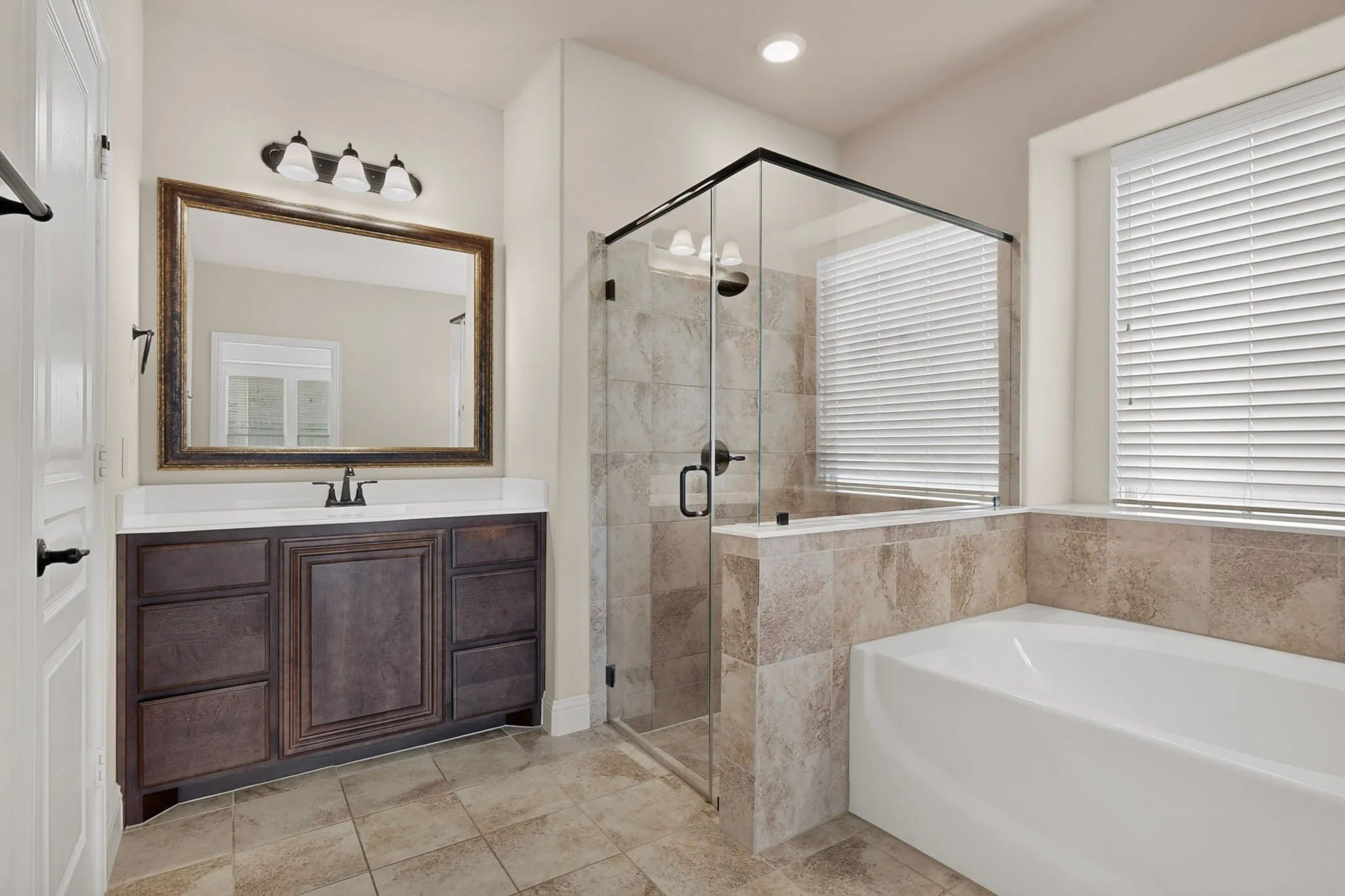 Spacious bathroom featuring a glass-enclosed shower, built-in soaking tub, and a dark wood-finish vanity with a white countertop