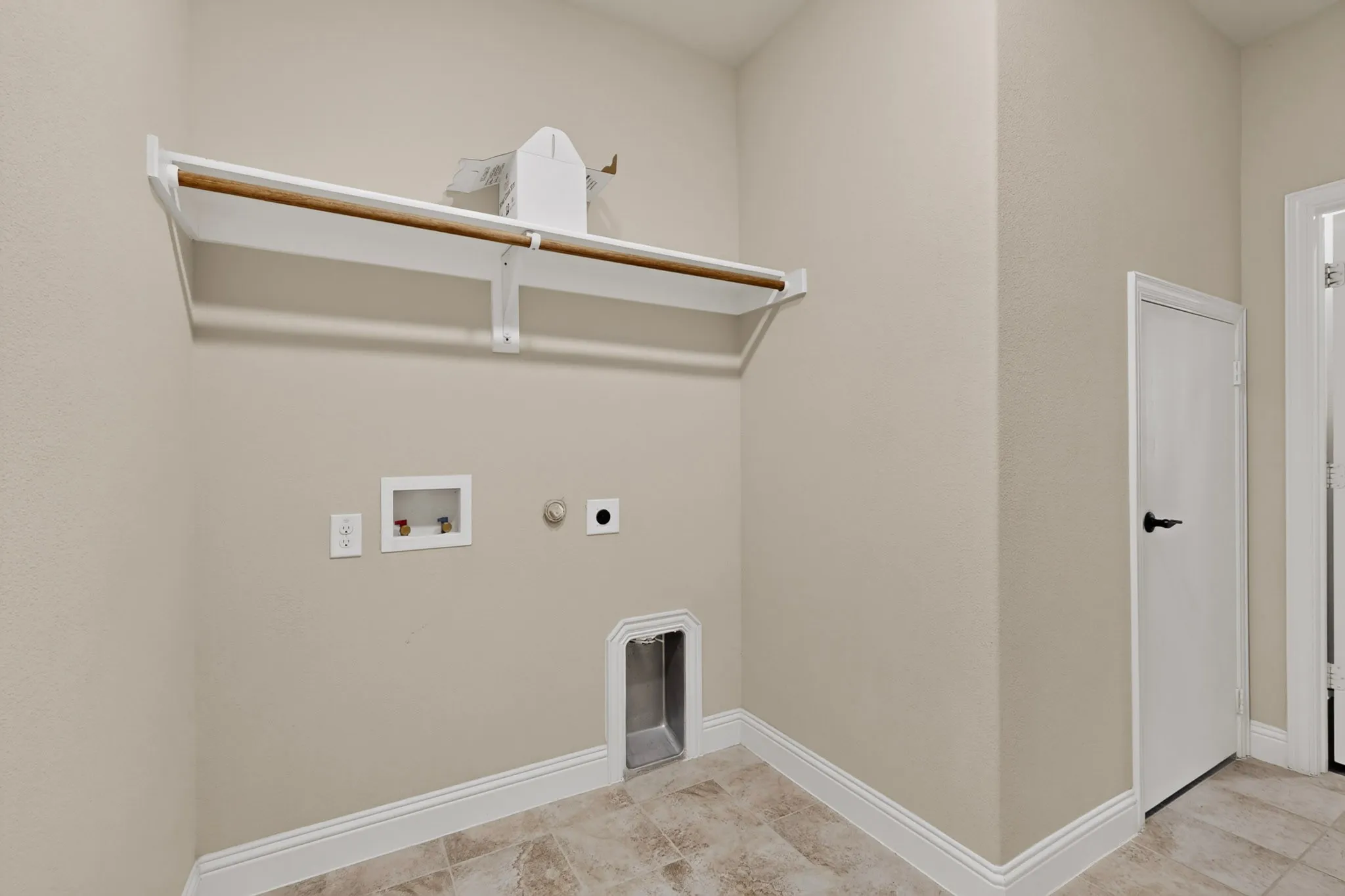Dedicated laundry area featuring a built-in hanging rod, wall-mounted shelf, and neutral-toned wall paint