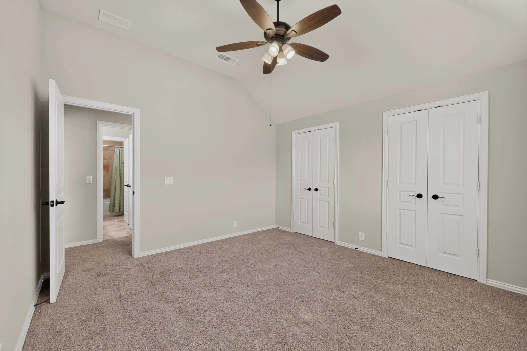 Spacious room featuring vaulted ceilings, a ceiling fan with integrated lighting, and neutral tone carpeting