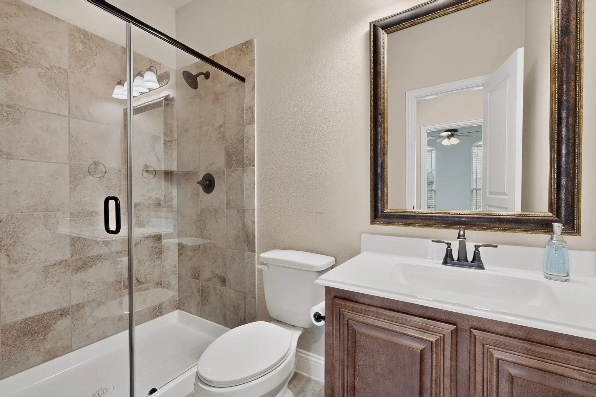 Shower with glass enclosure, textured tile surround, and matte black fixtures