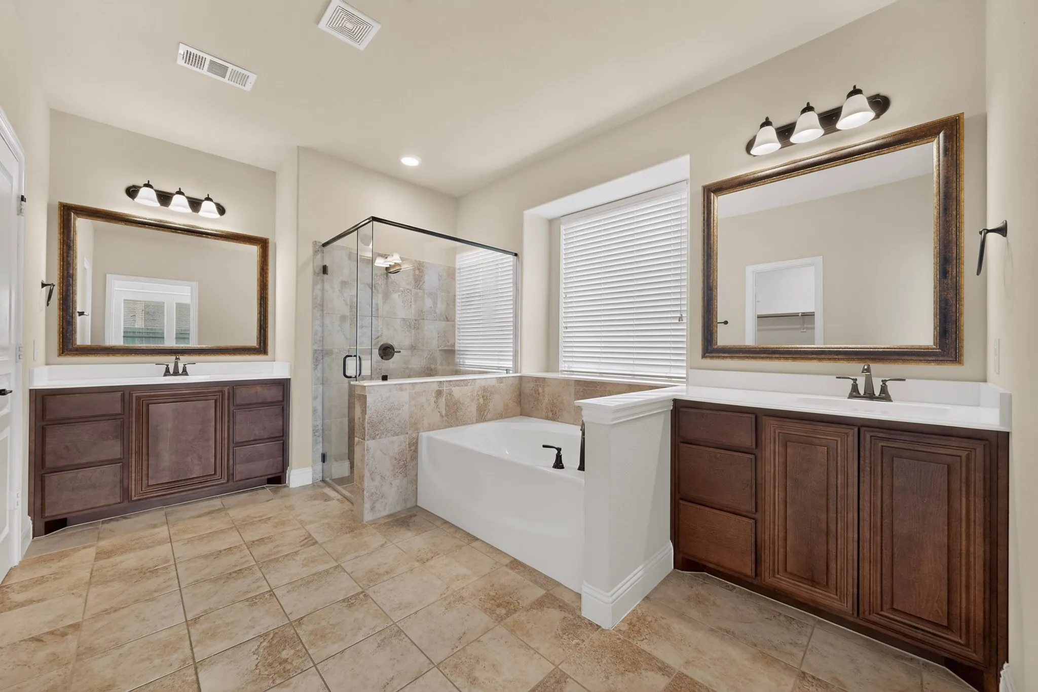 Spacious bathroom featuring dual vanities with dark wood cabinetry, a built-in soaking tub, a tiled walk-in shower with a glass enclosure, and large format tile flooring
