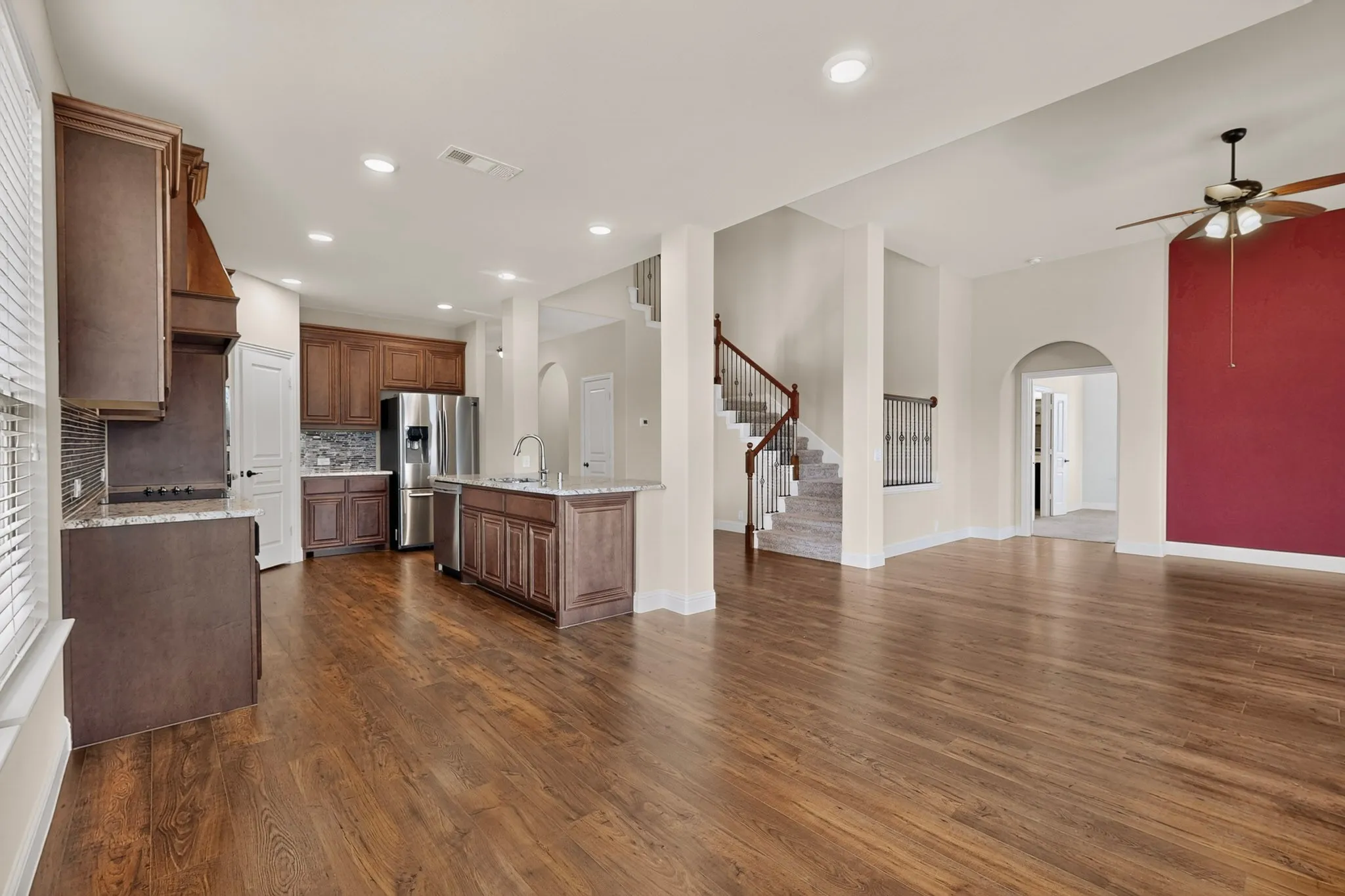 Open-concept living space featuring wood-finish flooring, recessed lighting, and a prominent staircase with wood railing
