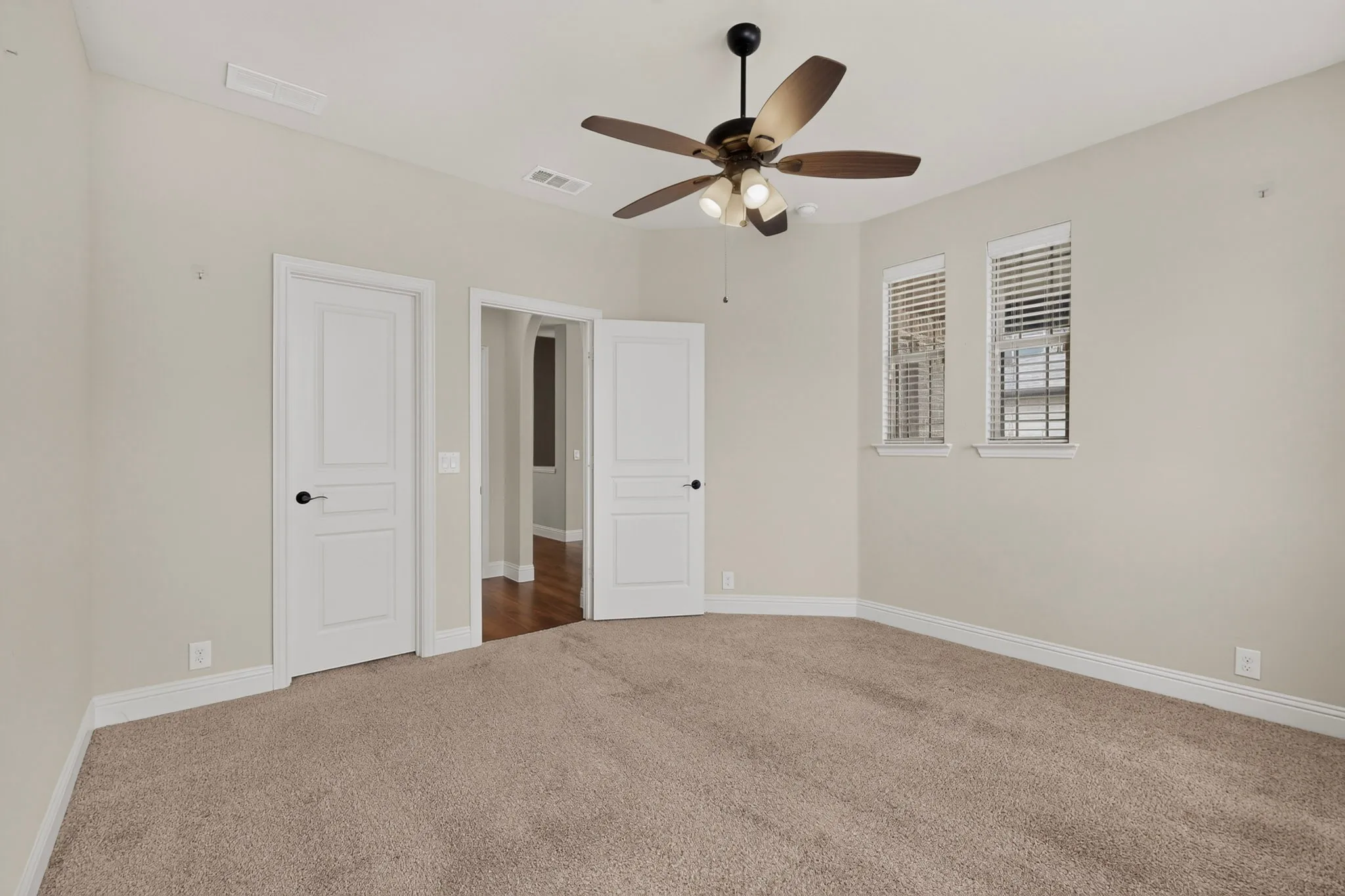 Carpeted interior room featuring a ceiling fan with integrated lighting, two windows with blinds, and white trim molding throughout