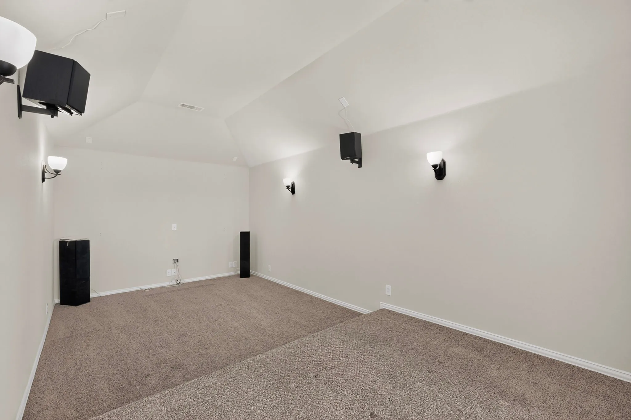 Theater room featuring tiered carpet flooring, vaulted ceiling, and built-in sconce lighting