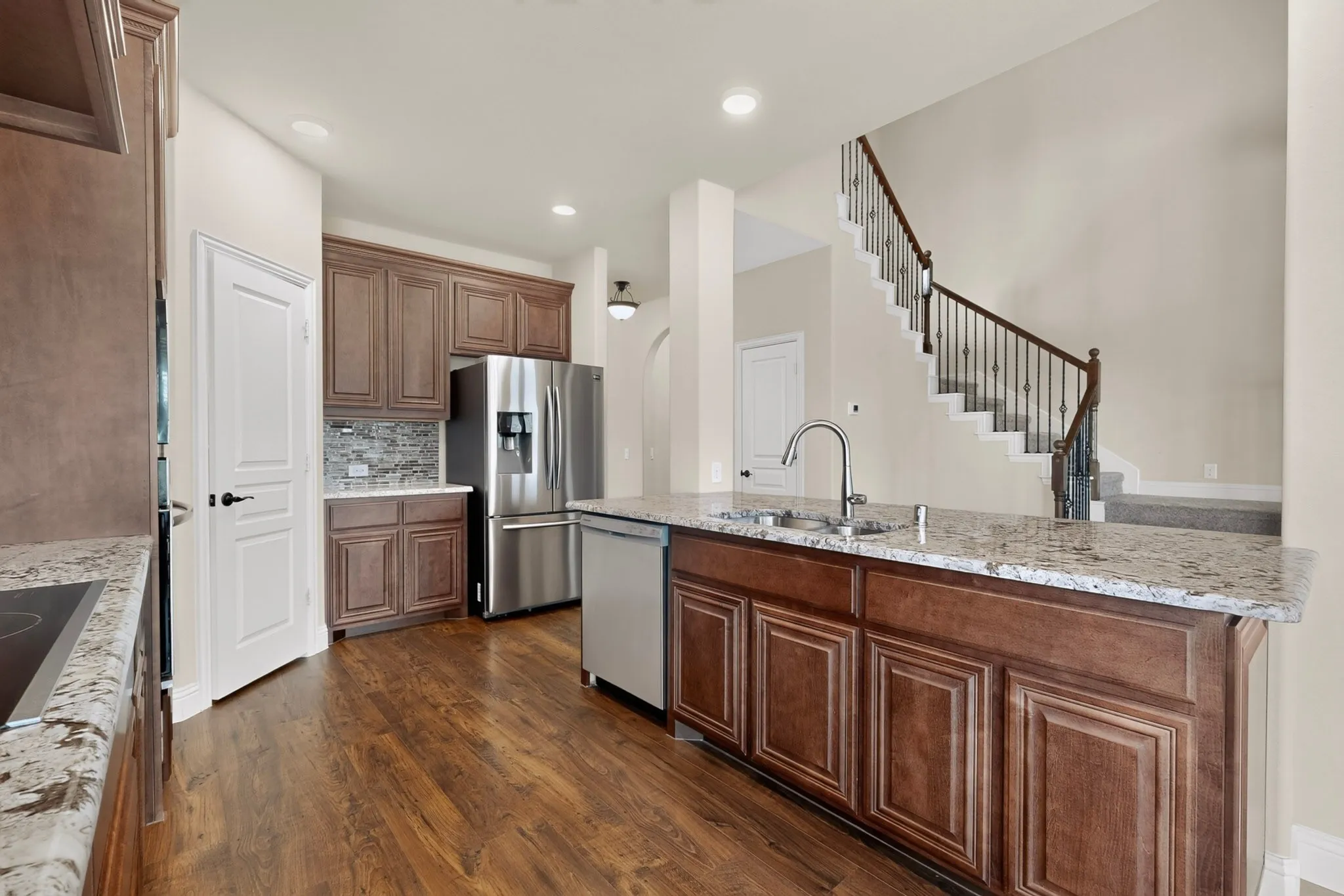Kitchen featuring wood-finish flooring, granite countertops, wood cabinetry, stainless steel appliances, and a tile backsplash