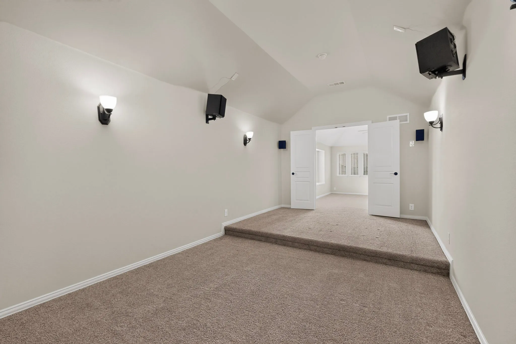 Carpeted room featuring a raised platform, vaulted ceiling, and white double doors