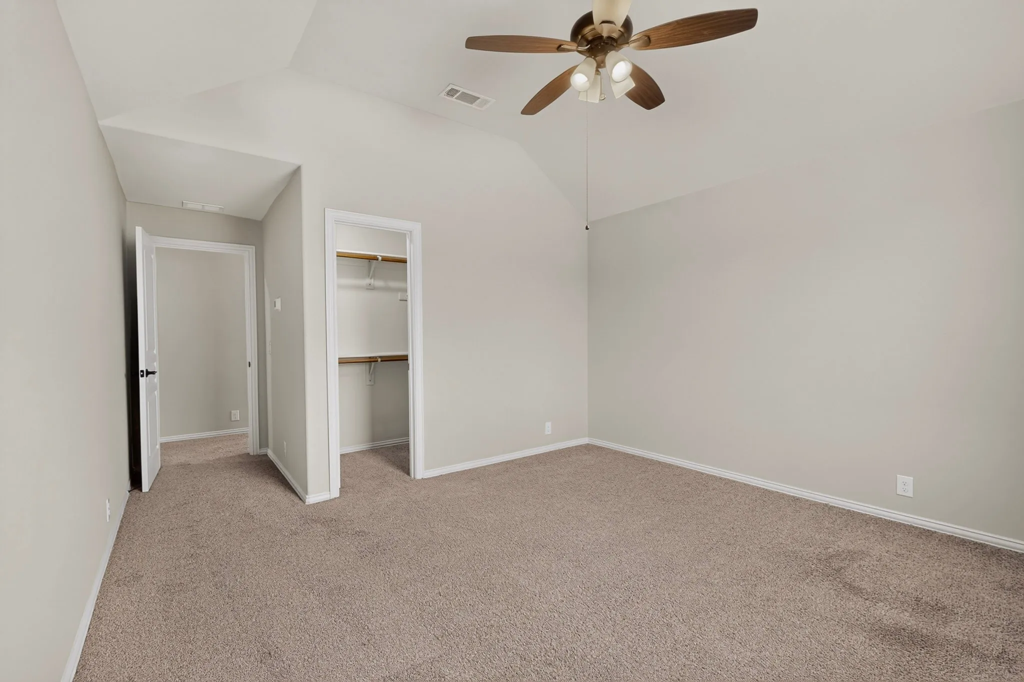 Spacious room featuring vaulted ceilings, neutral-toned carpeting, and a ceiling fan with integrated lighting