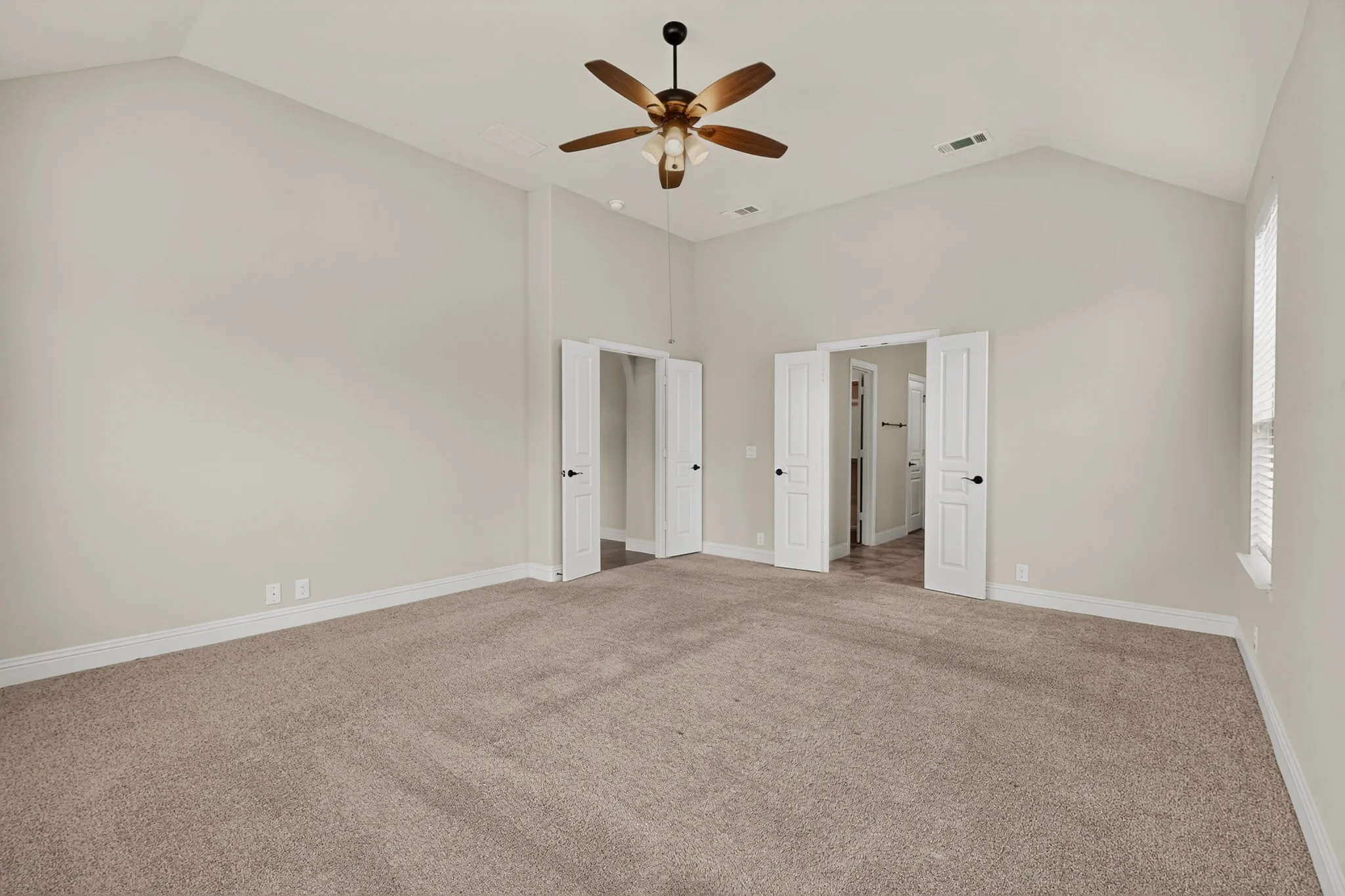 Spacious room featuring vaulted ceilings, neutral carpet flooring, a ceiling fan with integrated lighting, and white trim