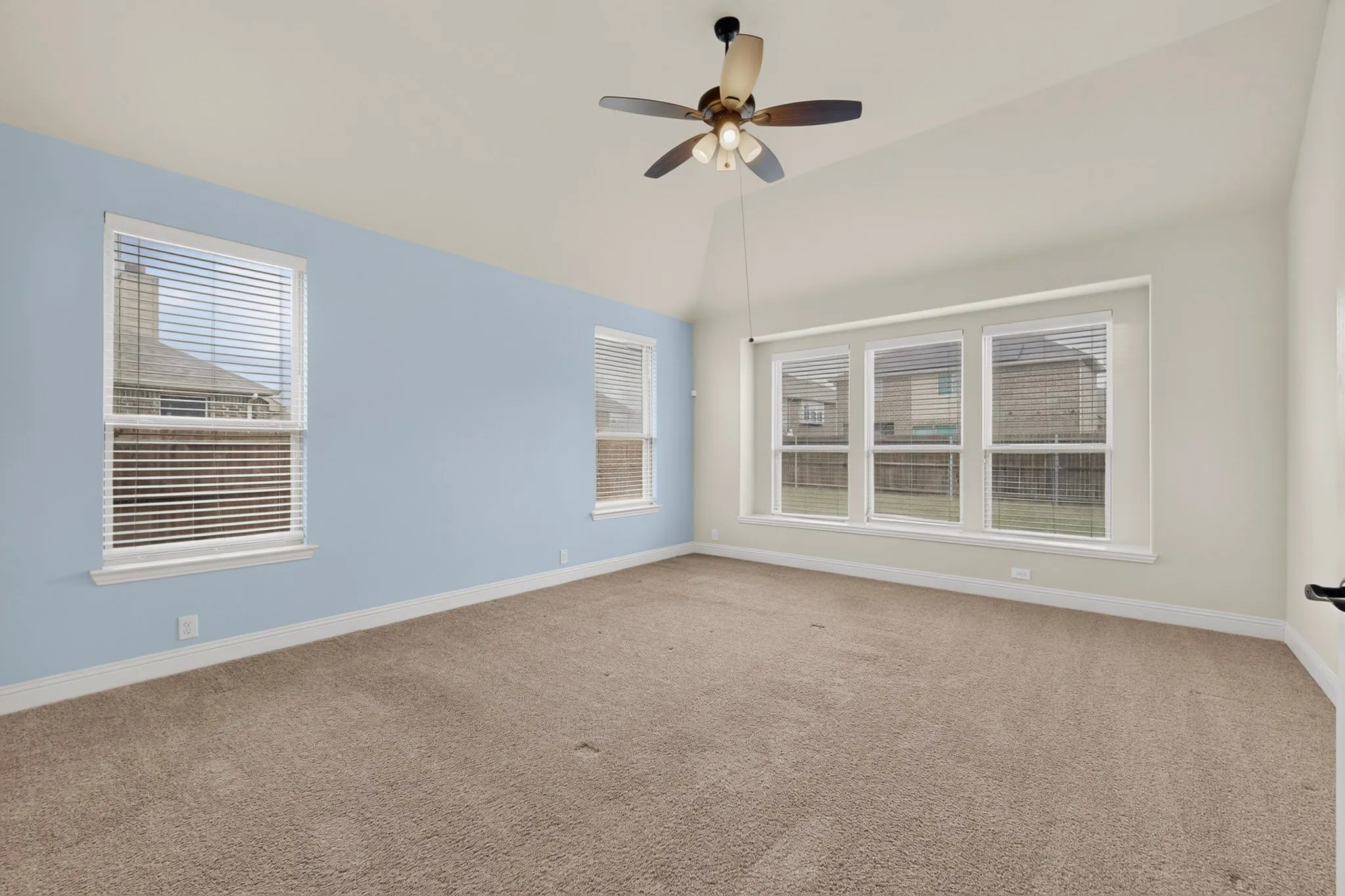 Spacious room featuring vaulted ceilings, a ceiling fan with integrated lighting, multiple windows with blinds, and​​‌​​​​‌​​‌‌​‌‌​​​‌‌​‌​‌​‌​​​‌​​ carpeting