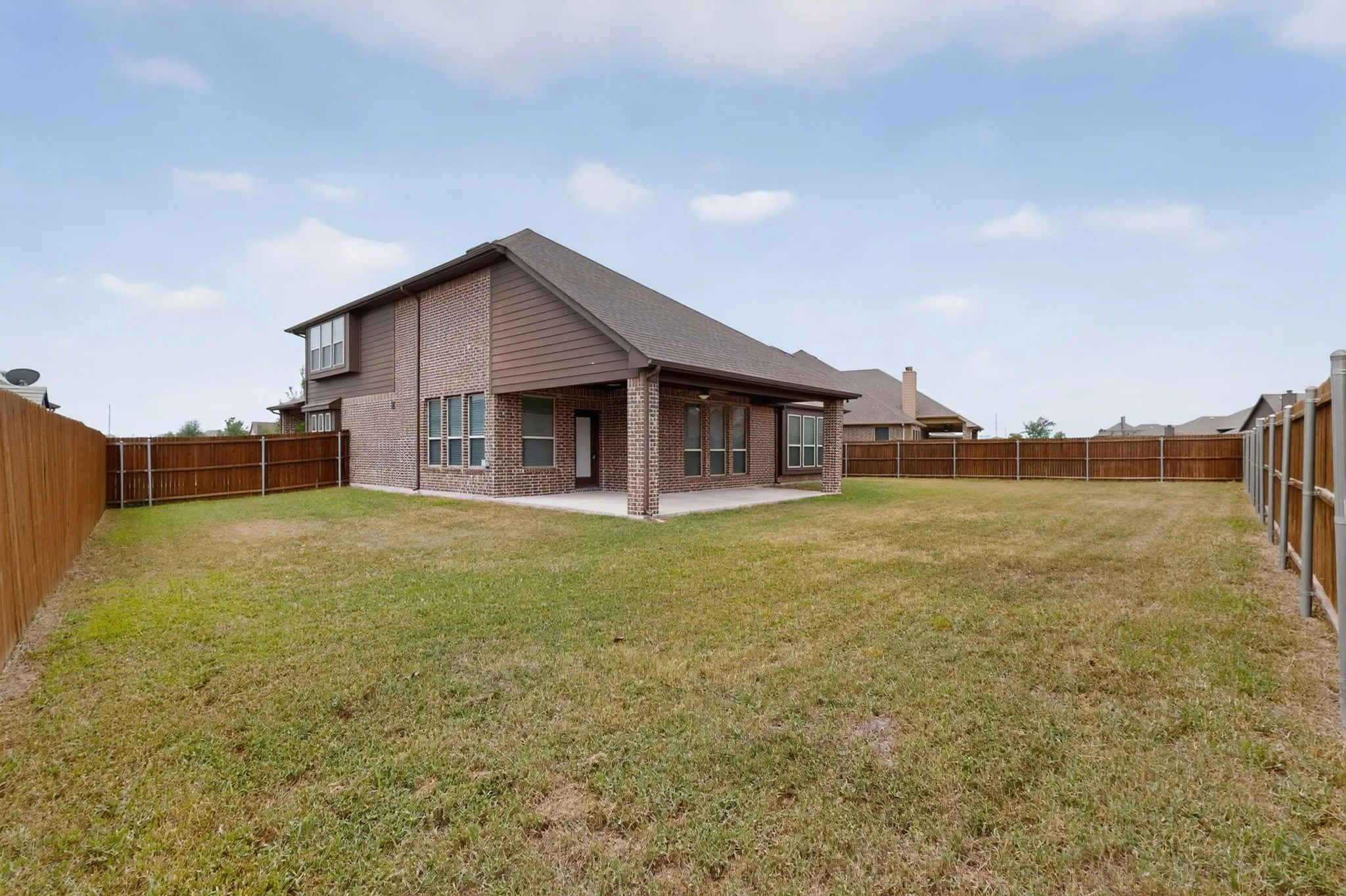 Expansive backyard featuring a covered patio, full privacy fencing, brick and siding exterior, and multiple windows