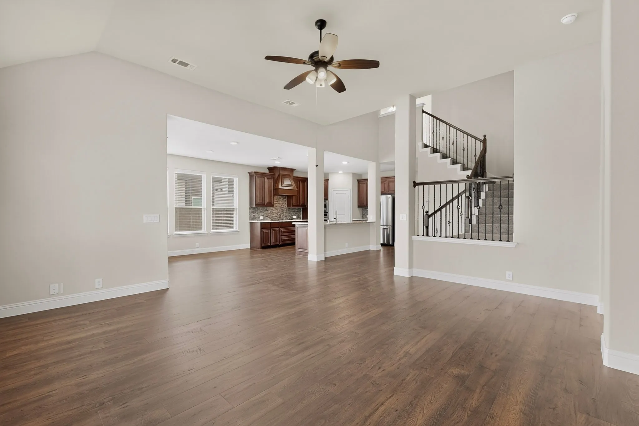 Spacious room featuring wood-finish flooring, vaulted ceilings, dramatic staircase and a ceiling fan with integrated lighting