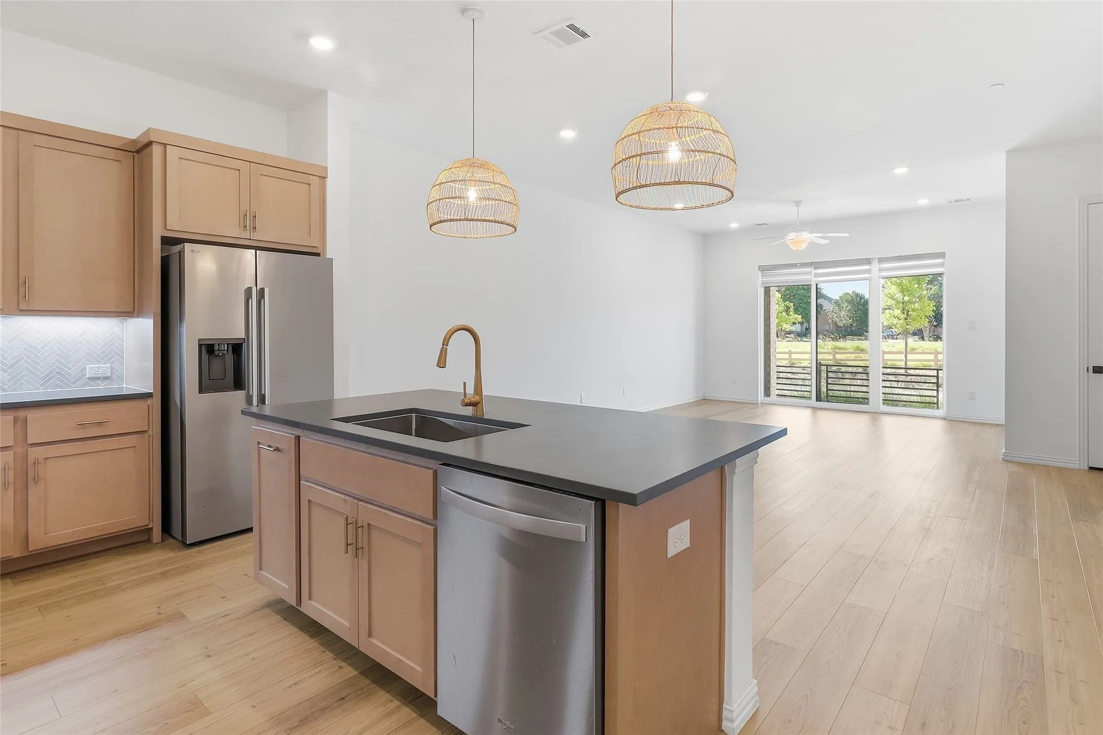 Open-concept kitchen featuring light wood cabinetry, stainless steel appliances, and a dark countertop island with an integrated sink