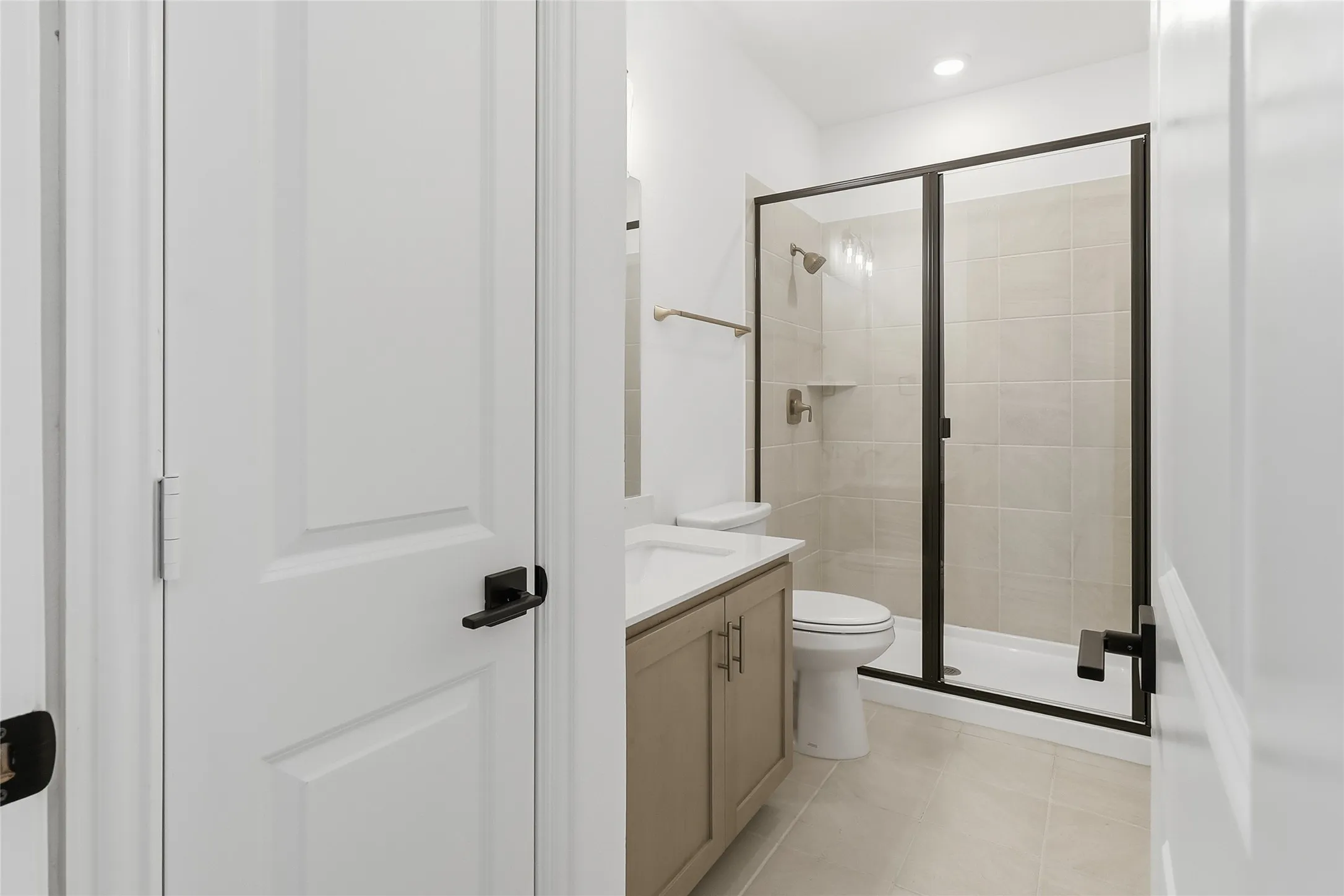 Full bathroom featuring a glass-enclosed shower with tiled walls and a built-in shelf, light-colored floor tiling, a vanity with cabinet storage, a white countertop, and a modern toilet
