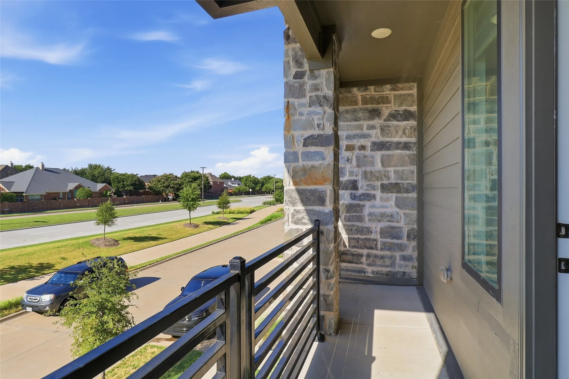 Exterior balcony with horizontal metal railings, a stone accent wall, and a recessed ceiling light