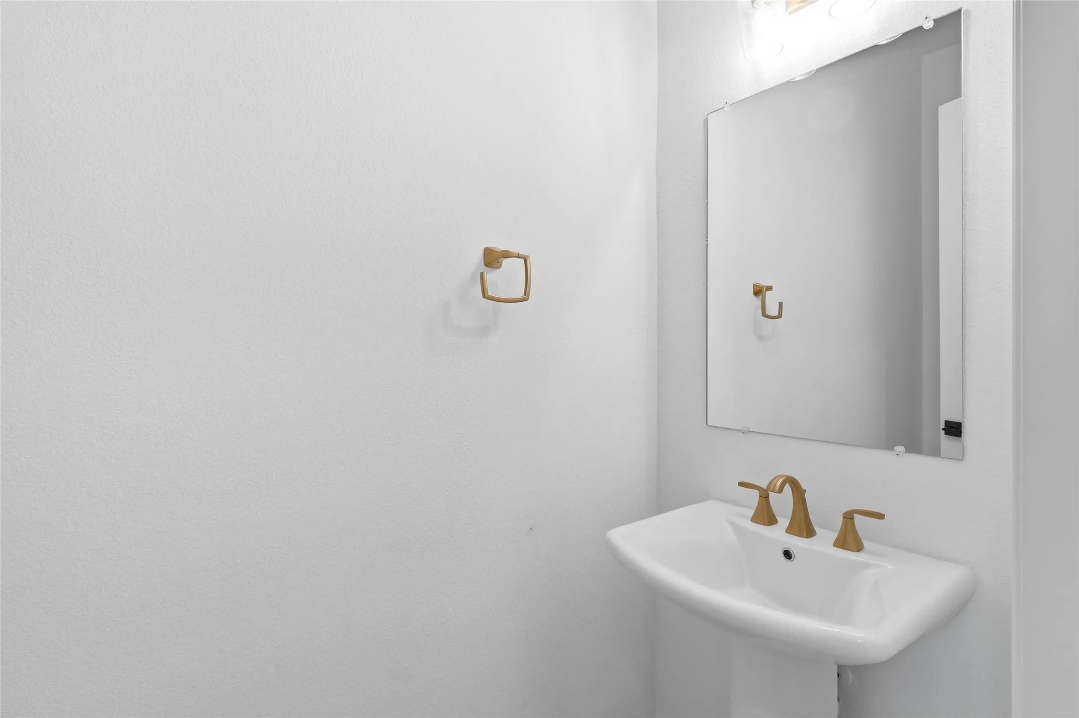 Pedestal sink with brass-finish faucet, rectangular mirror, and overhead vanity lighting