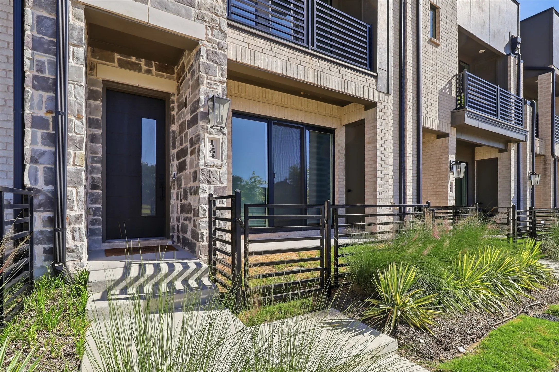 Modern townhome exterior featuring a stone and brick facade, dark-frame windows, and a sleek entry door with a vertical glass insert